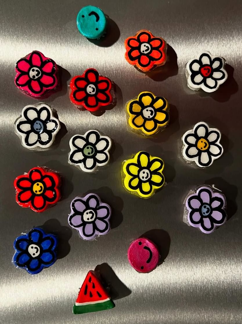 Colorful flower-shaped beads, a watermelon slice, and a blue smiley face on a metallic surface.