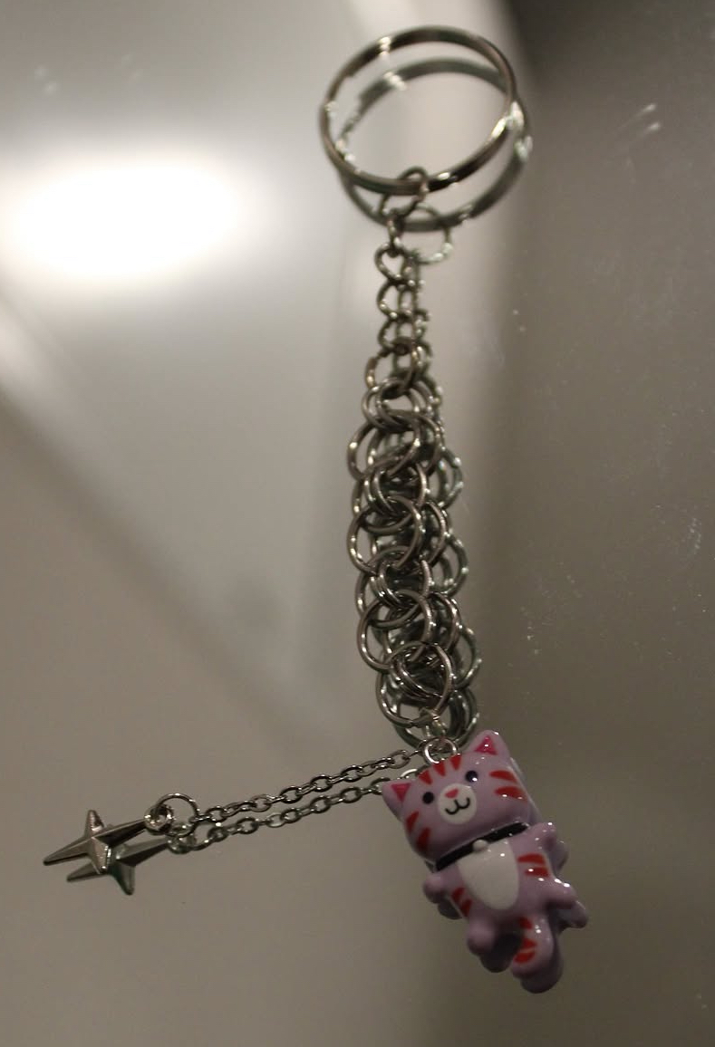 Keychain with a pink cat figure, star charm, and chain, hanging against a reflective surface.