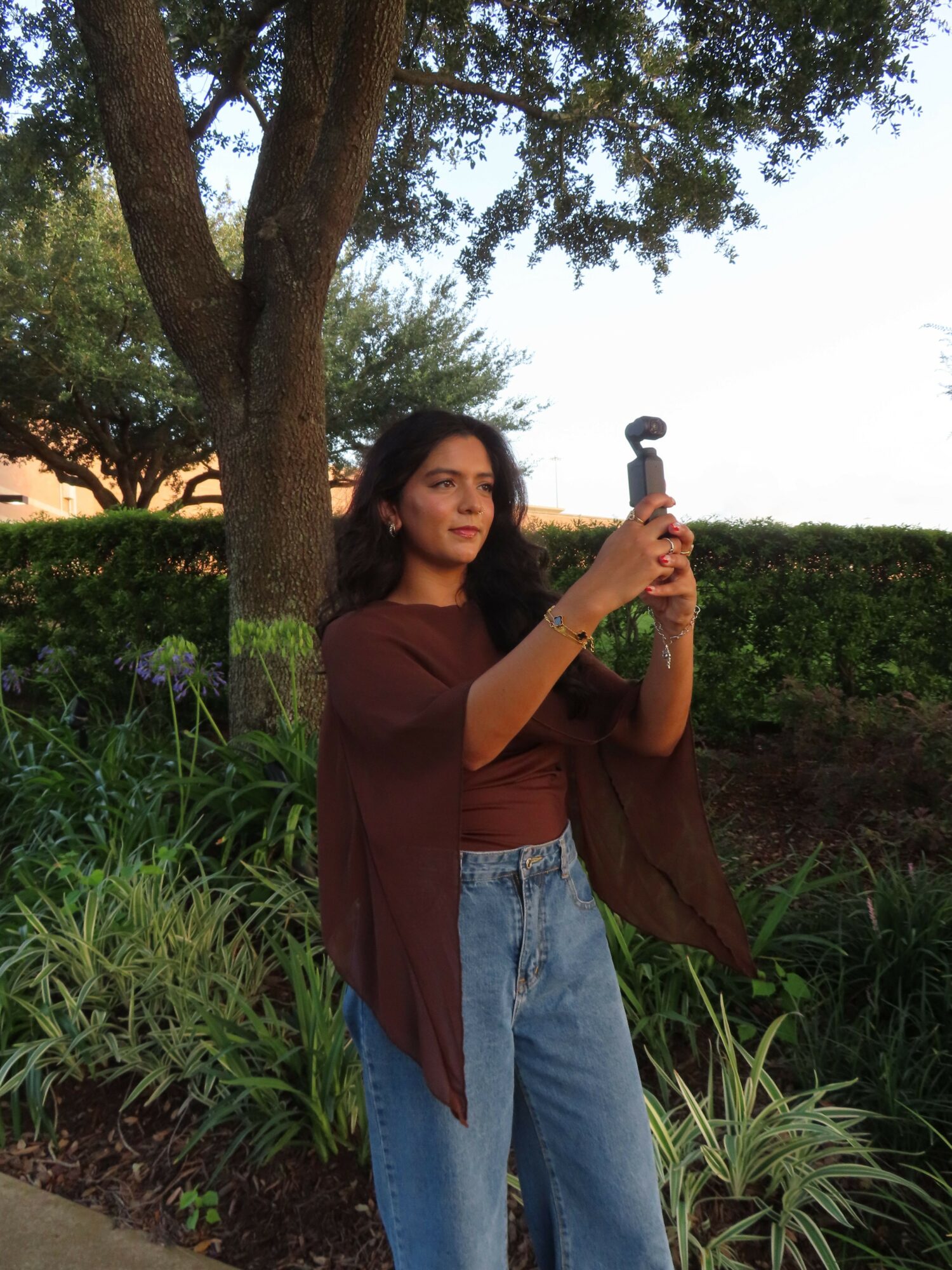 Woman holding a hammer outdoors near trees and greenery, smiling, during sunset.