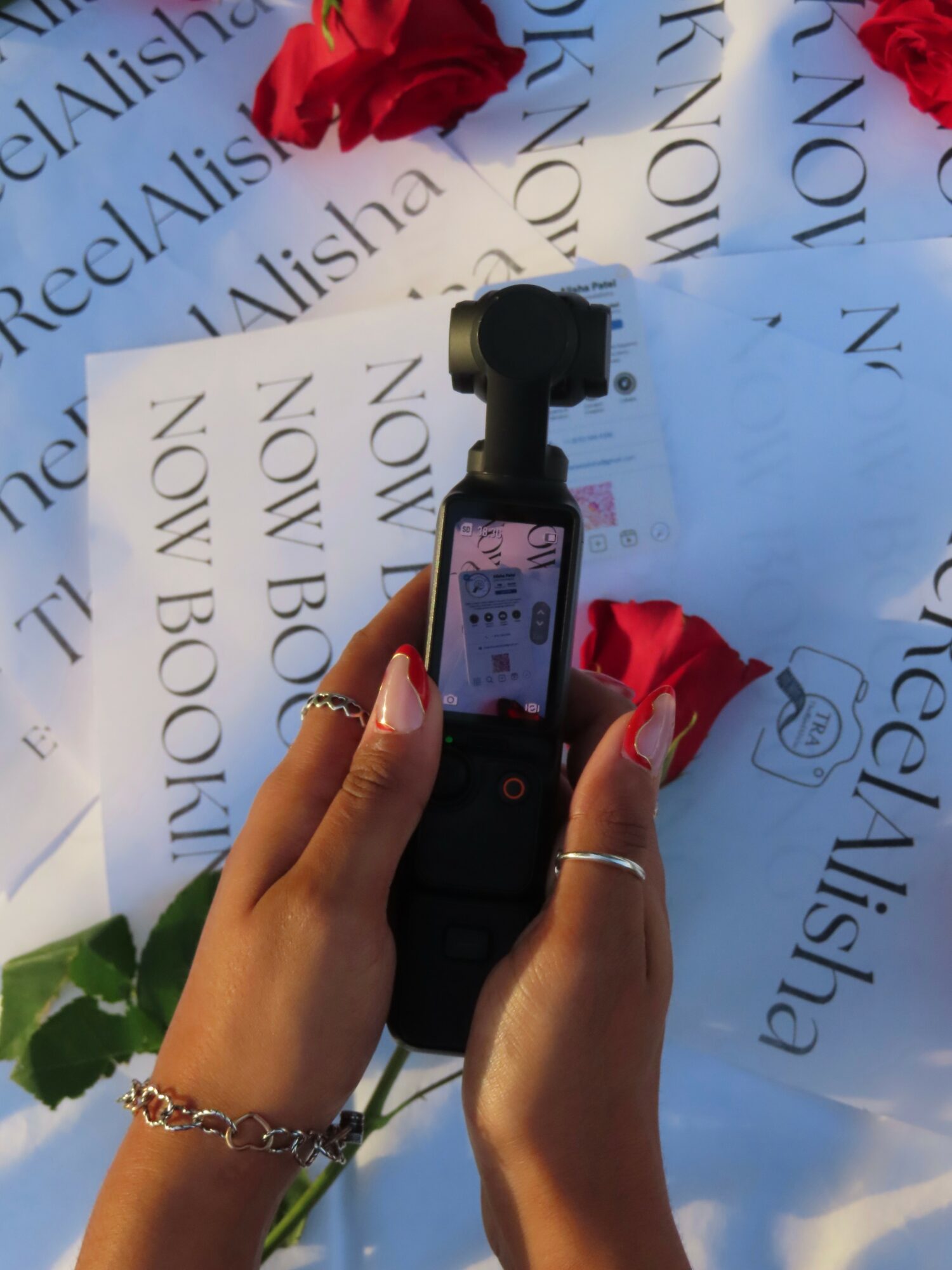 Person holding a camera with a screen, surrounded by red roses and printed papers, some with text.