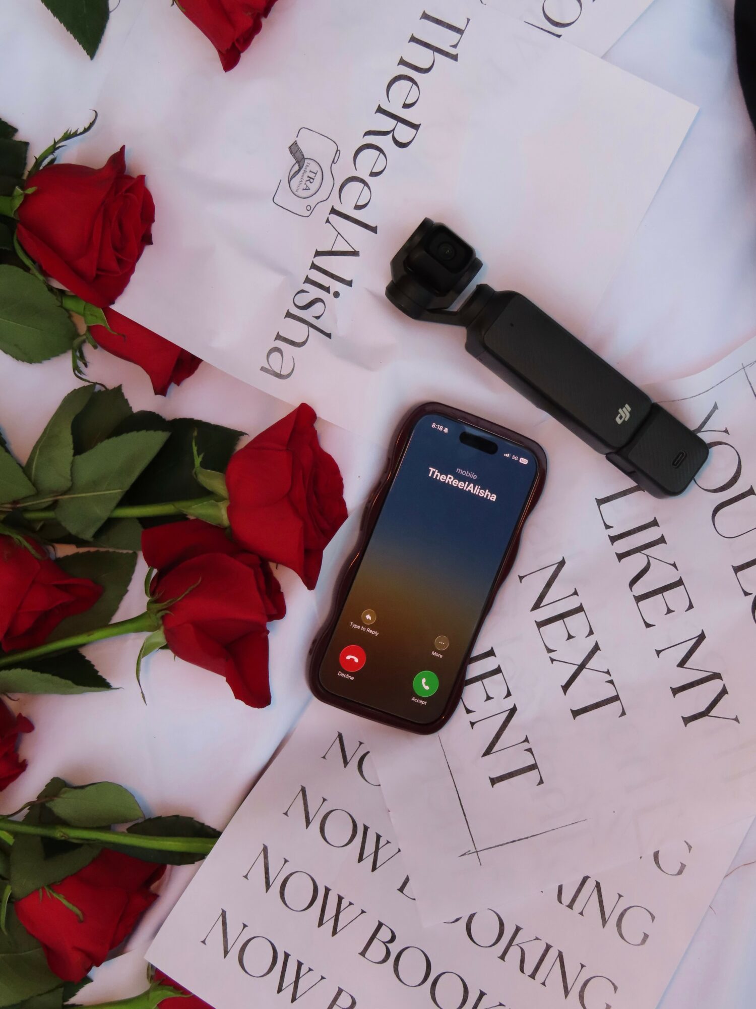 Smartphone with a call screen, surrounded by red roses and papers with text, on a white surface.