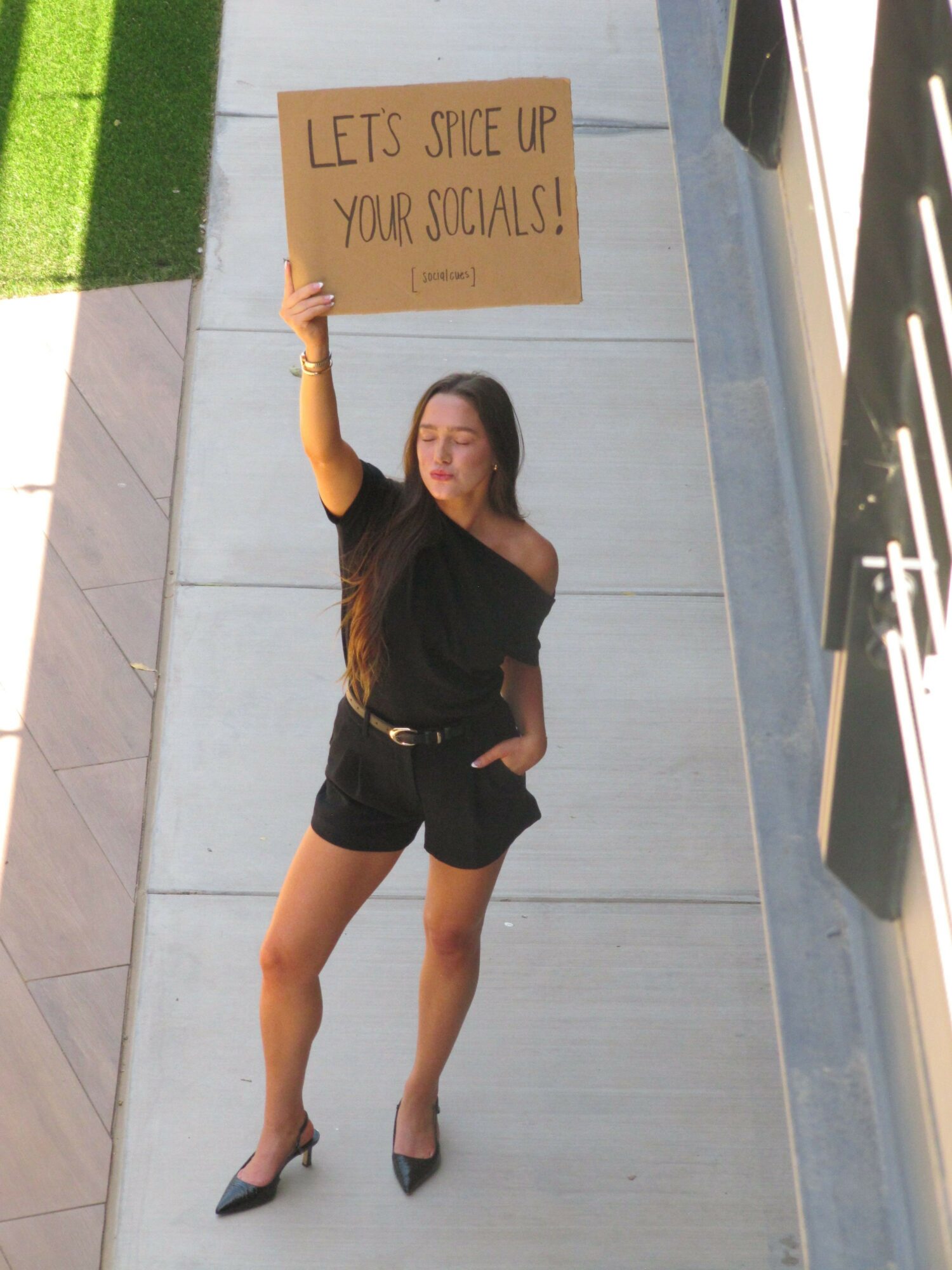 Woman standing on sidewalk holding a sign that reads 'Let's sit up, you could!'.