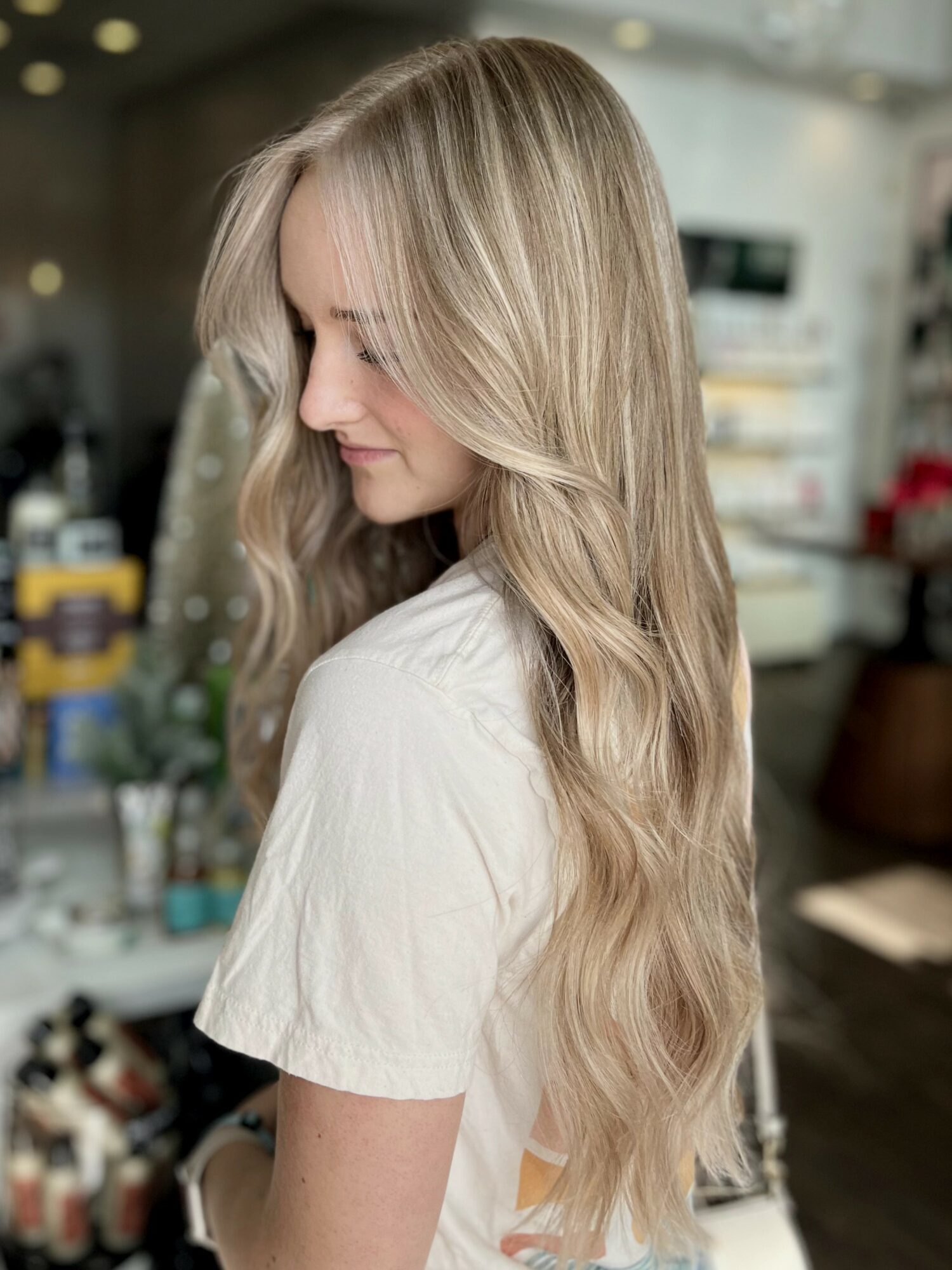 Woman with long, wavy blonde hair looking down in a room with shelves and various items