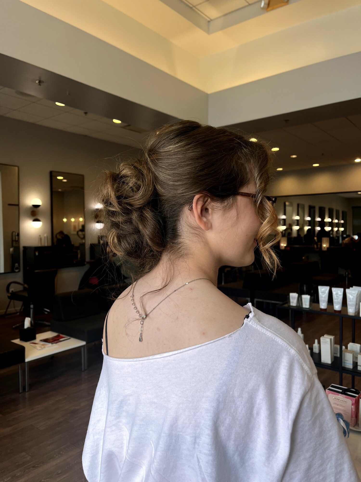 Side view of a woman with styled hair and glasses, wearing a white top, in a modern interior space.