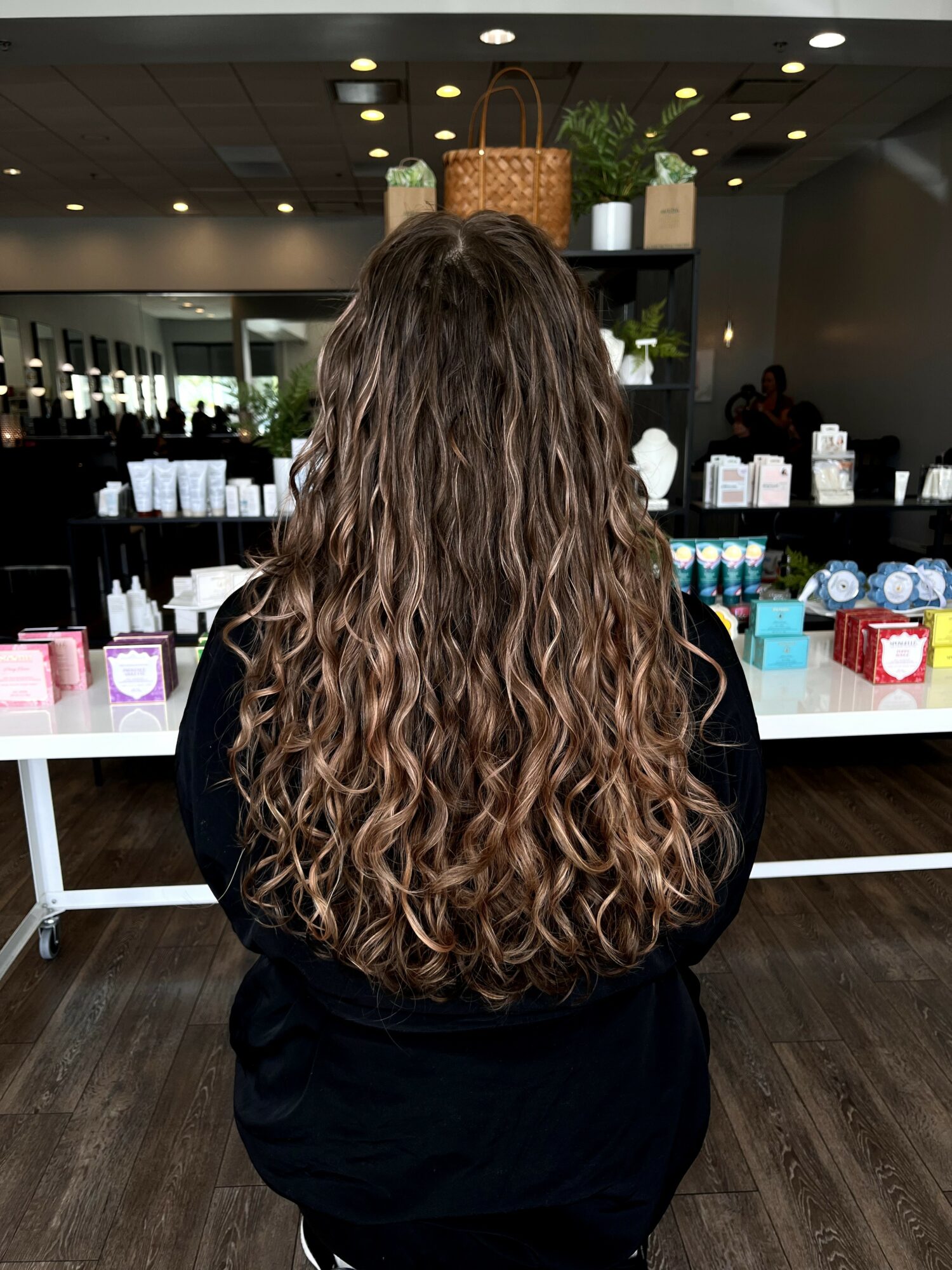 Person with long, curly hair standing in front of a display of beauty products in a store.