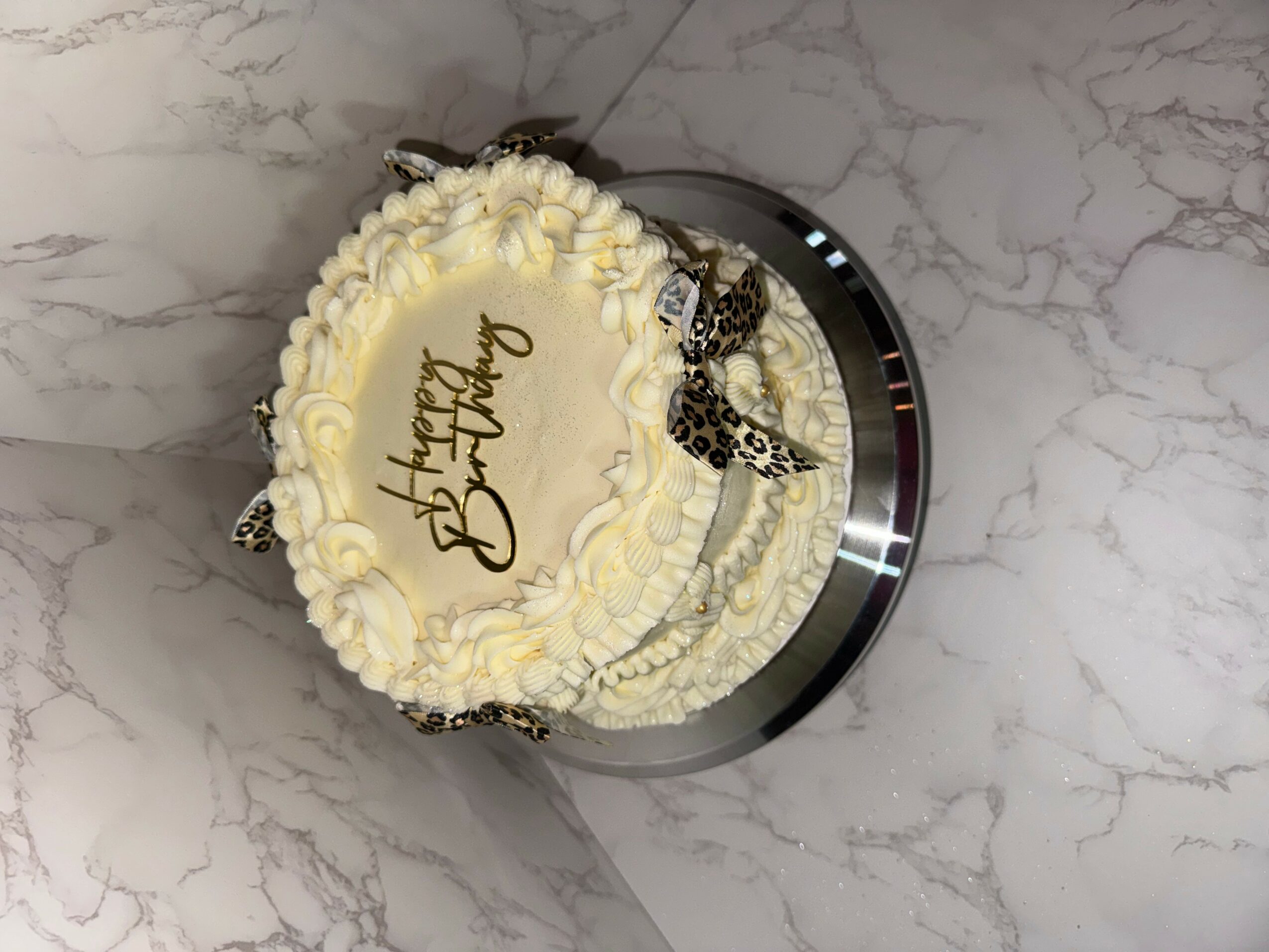 Round birthday cake with white frosting, chocolate decorations, and a message, on a marble surface.