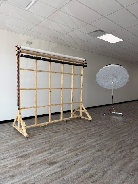 Studio setup with a wooden frame, a large umbrella light, and a white ceiling with a light fixture.