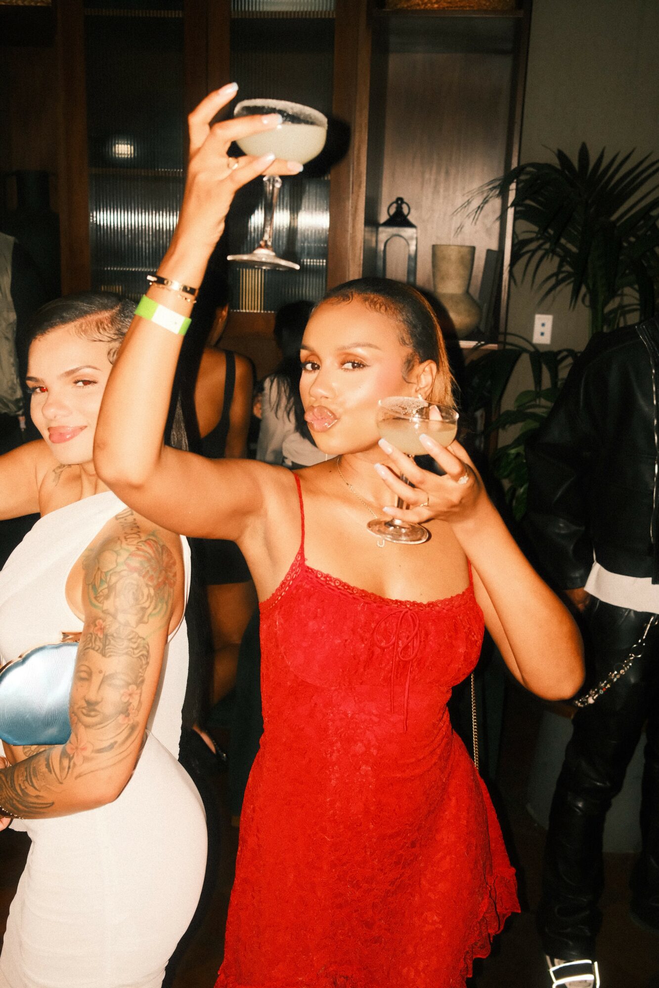 Woman in red dress holding a cocktail glass at a party, with another person partially visible beside her.