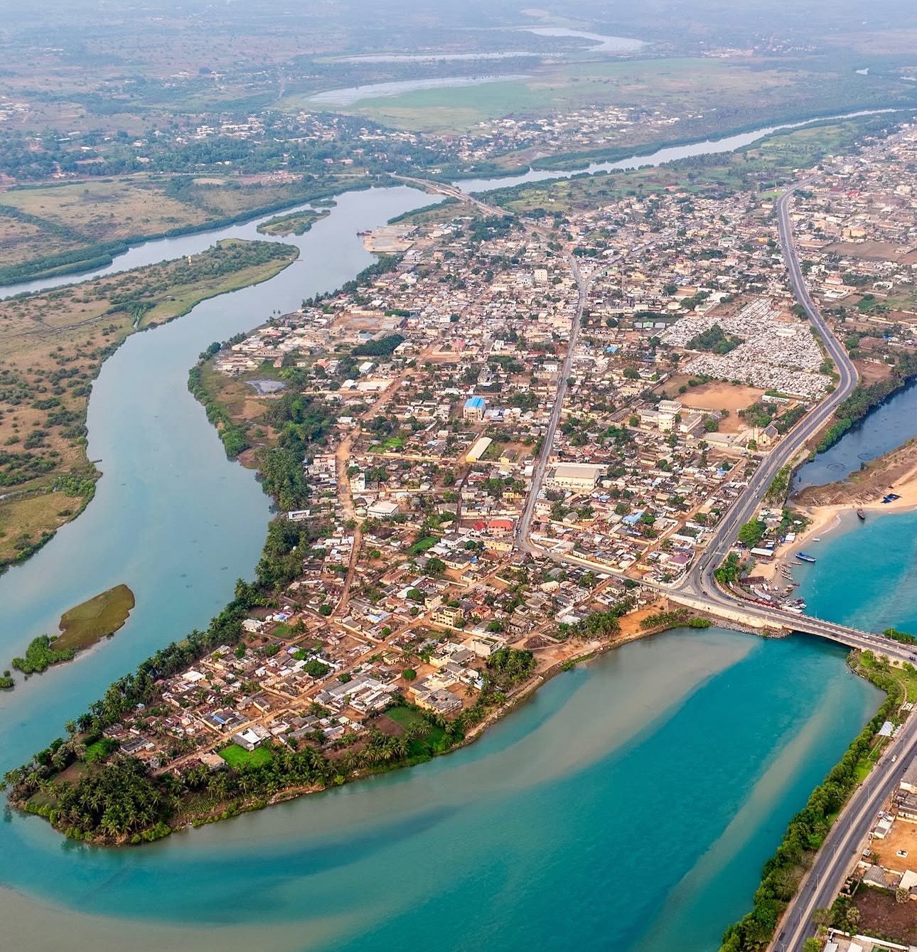 Aerial view of a city with rivers, roads, and buildings, showing a peninsula surrounded by water and a bridge crossing a river.