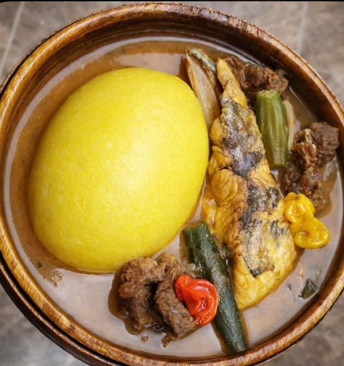A bowl with a large yellow lemon, fish, vegetables, and condiments, viewed from above.