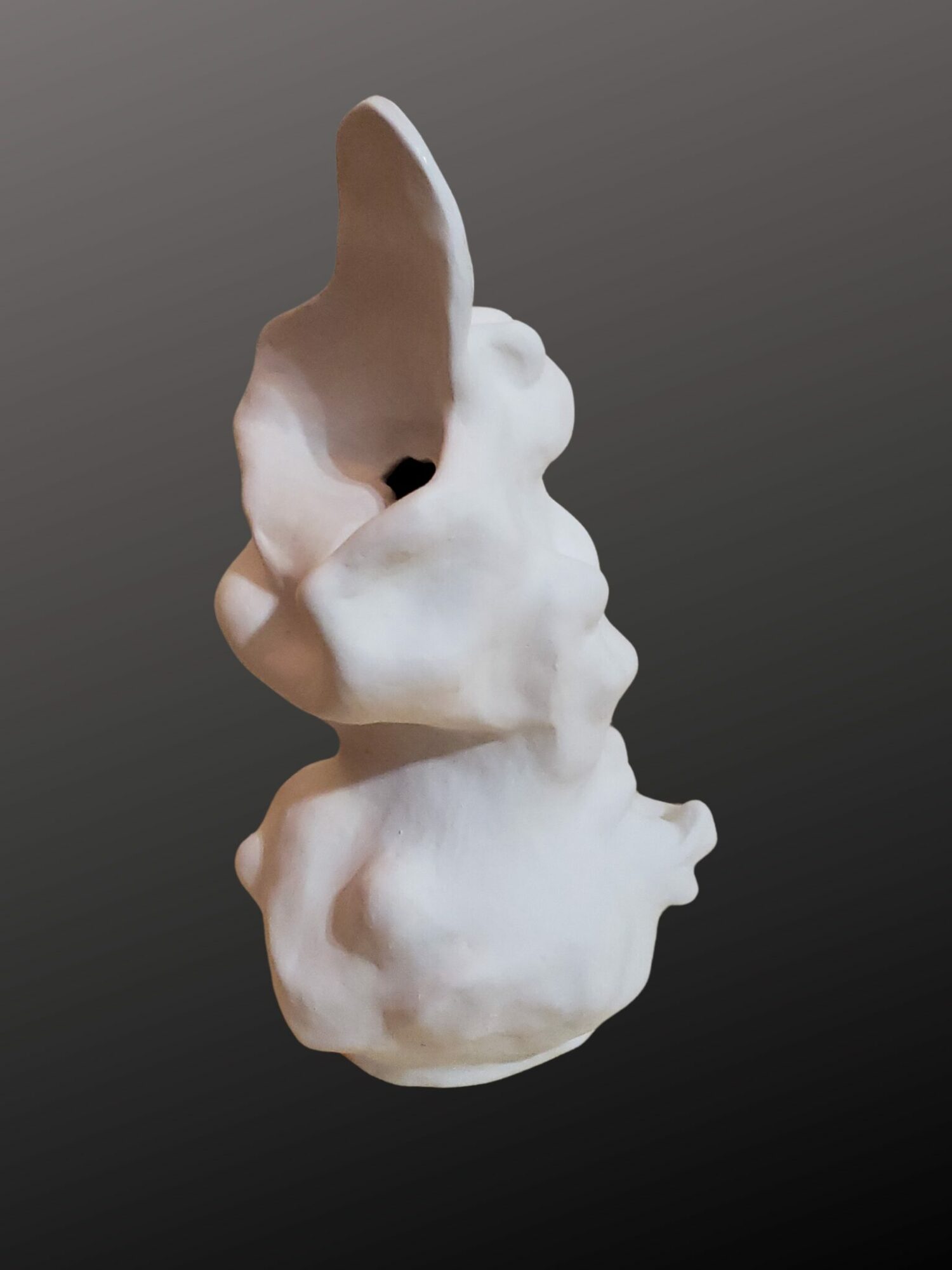 White ceramic rabbit sculpture with large ears and a hollow interior, set against a dark background.