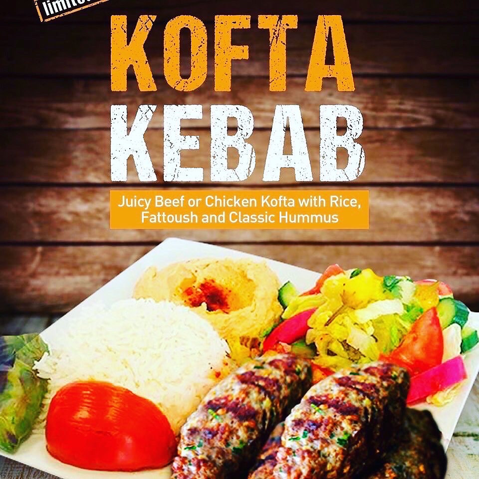 Plate with rice, kebabs, tomato, and salad against wooden background, advertising Kofta Kebab dish.