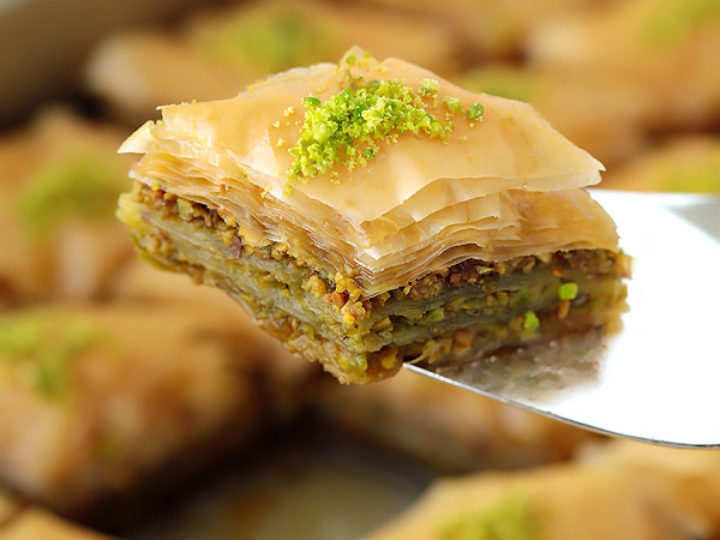 Close-up of a layered pastry with green garnish on top, on a reflective surface.