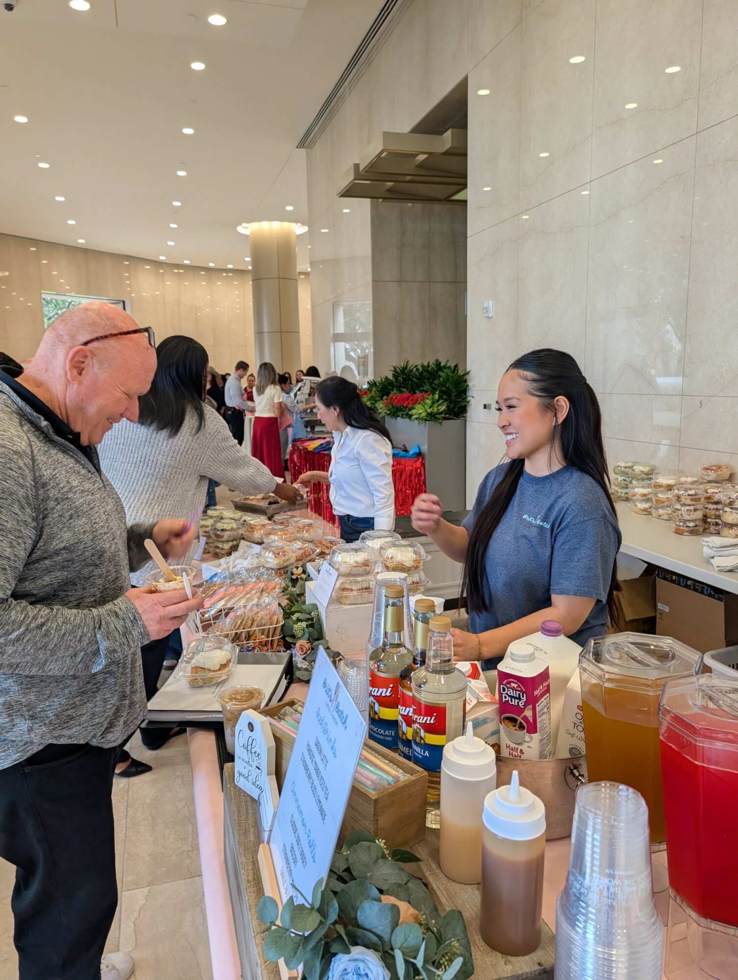A woman serving food to a man at a buffet table in a spacious, well-lit indoor setting with other people in the background.