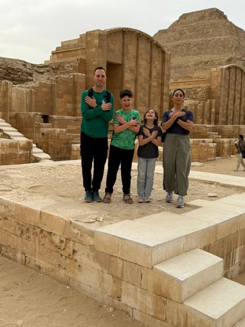 Four people stand on a stone platform in front of ancient stone ruins, posing for a photo.