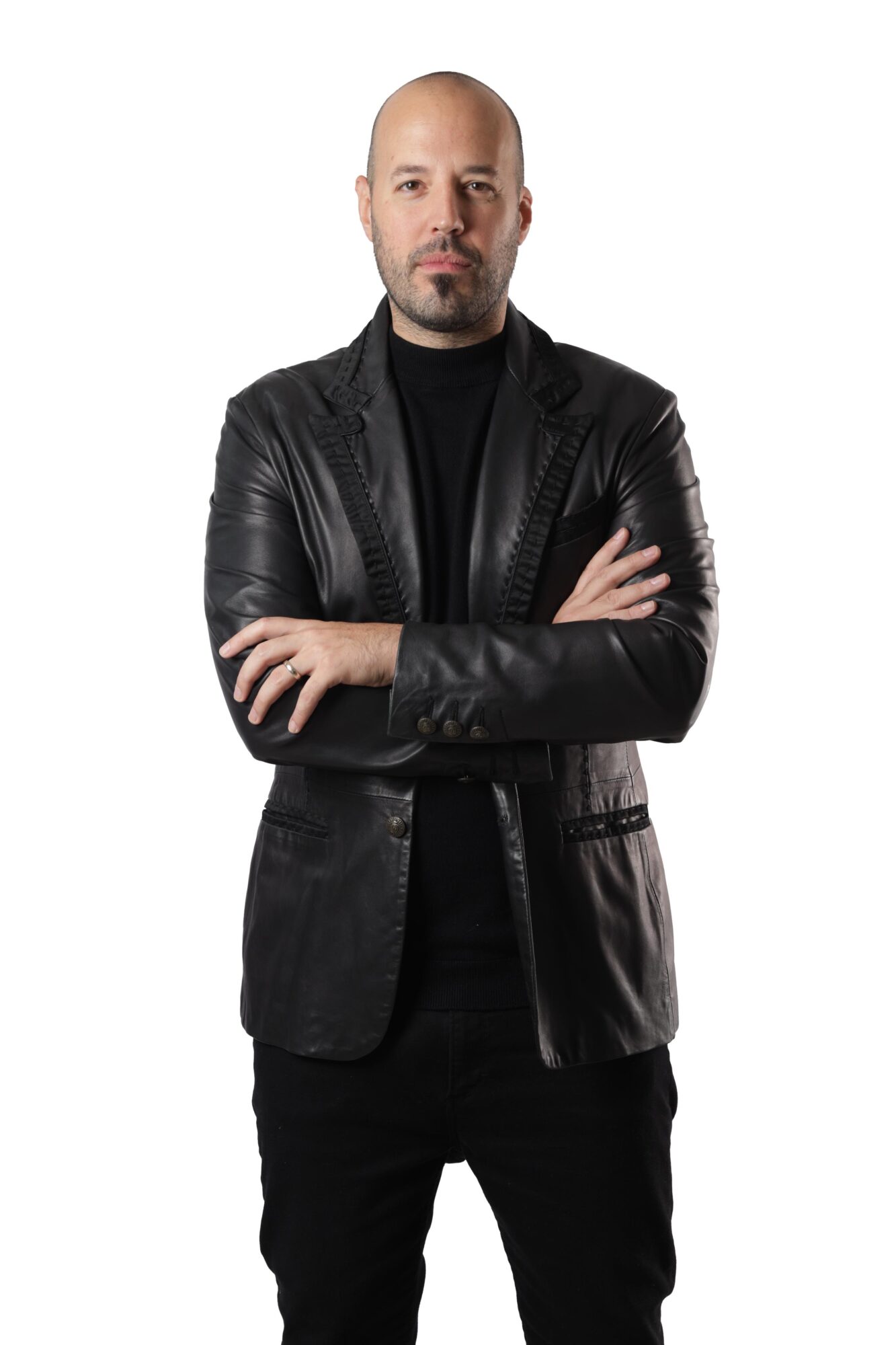 Man with a bald head and beard wearing a black leather jacket and black shirt, arms crossed, against a white background.