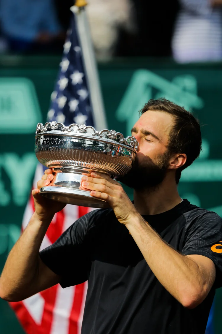 Man kissing a large silver trophy with an American flag in the background, celebrating victory.