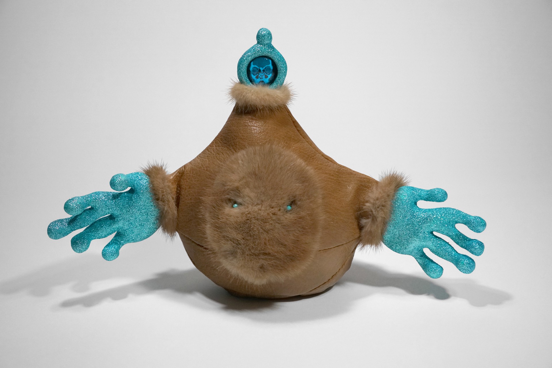 Round plush toy with blue gloves, a blue hat, and a small blue figure on top, against a plain background.