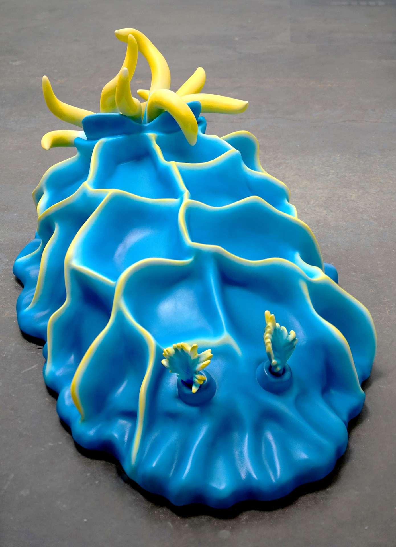 Colorful inflatable pool float shaped like a pineapple with yellow top and blue body, on a gray surface.