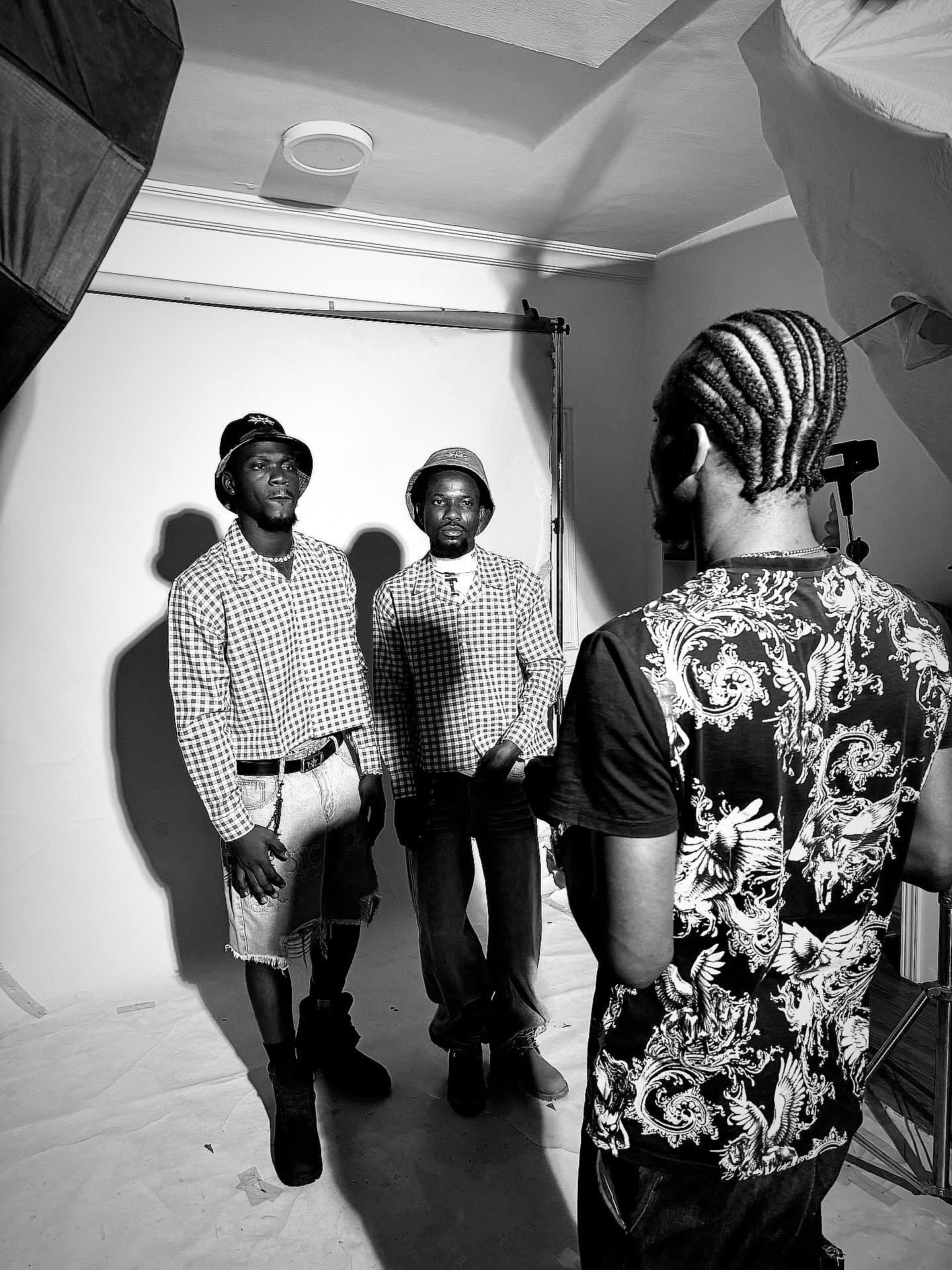 Two men stand in front of a white backdrop, posing for a photo, with a person taking their picture in a studio.