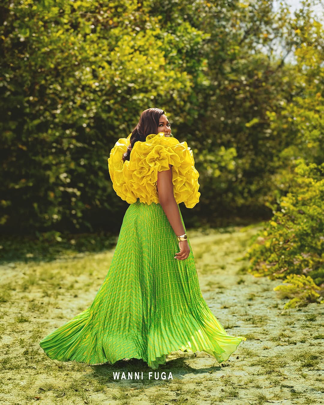 Woman in a bright green pleated skirt and yellow top walking outdoors with trees in background.