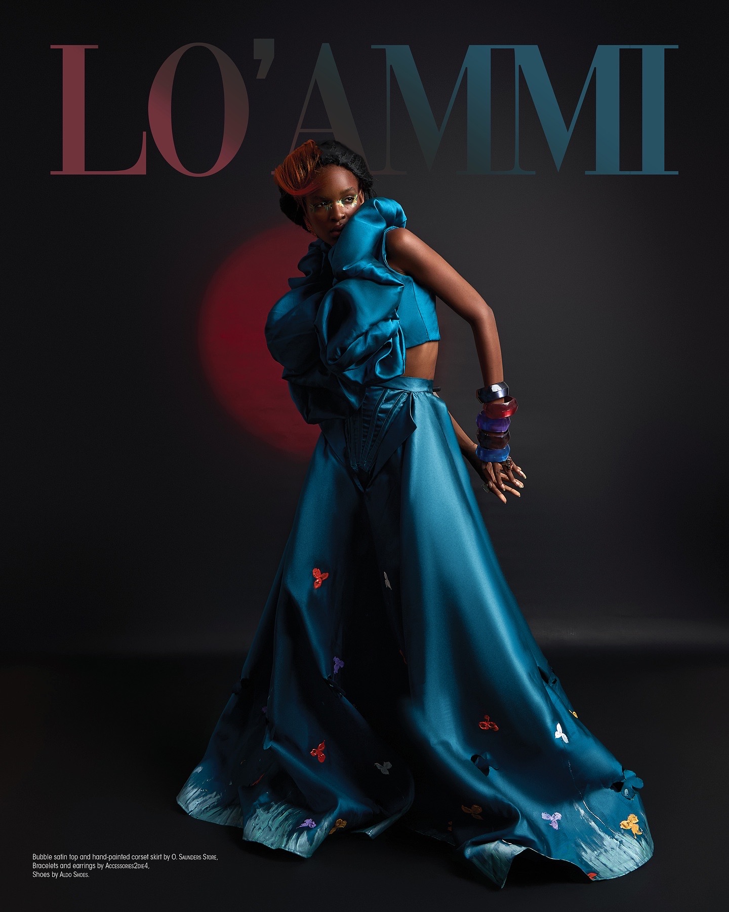 A woman in a flowing blue dress with accessories poses against a dark background, with text 'L'OAMMI' above her.