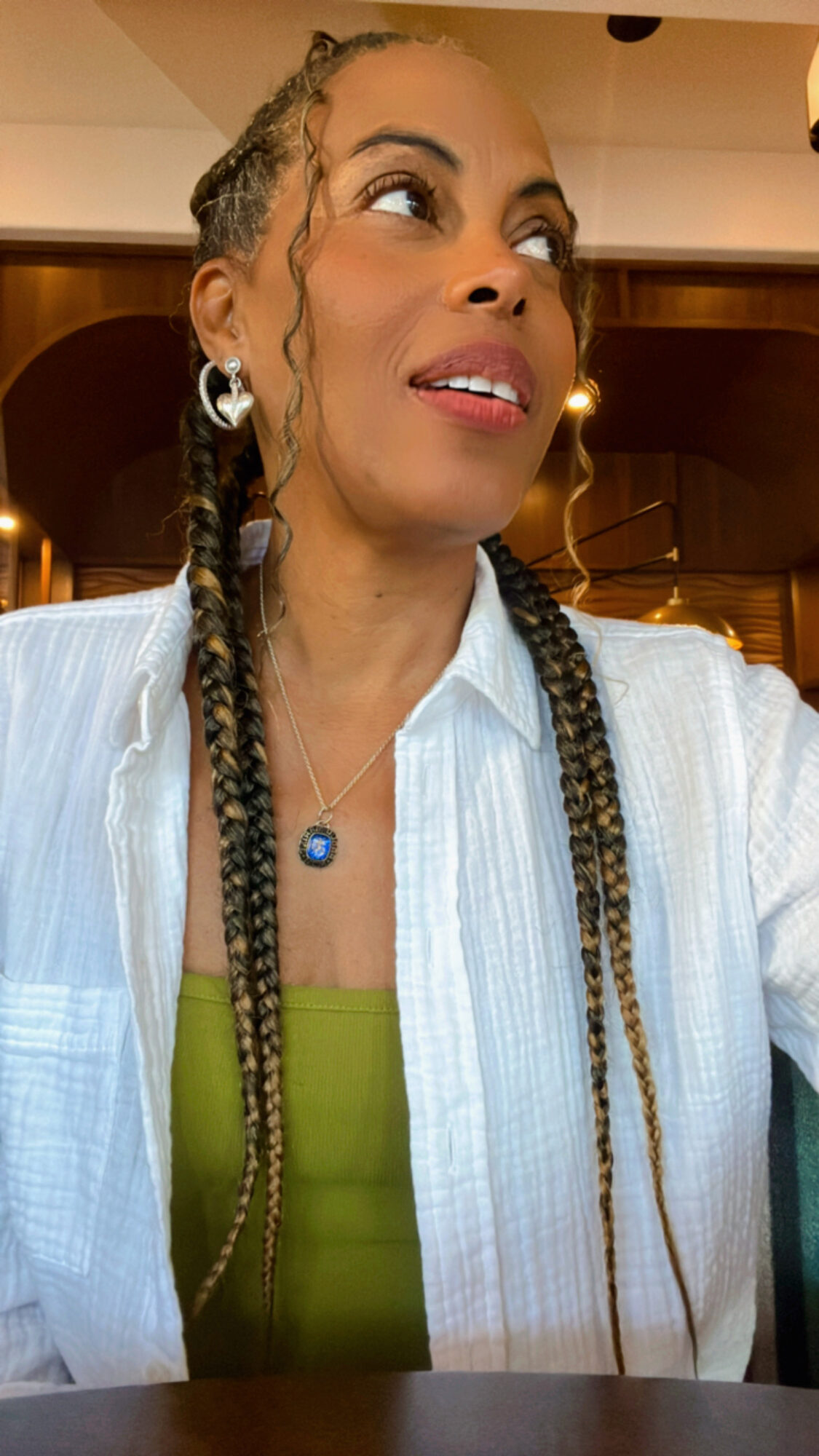 Woman with braided hair wearing earrings and a white shirt, looking to the side in a warmly lit indoor setting.