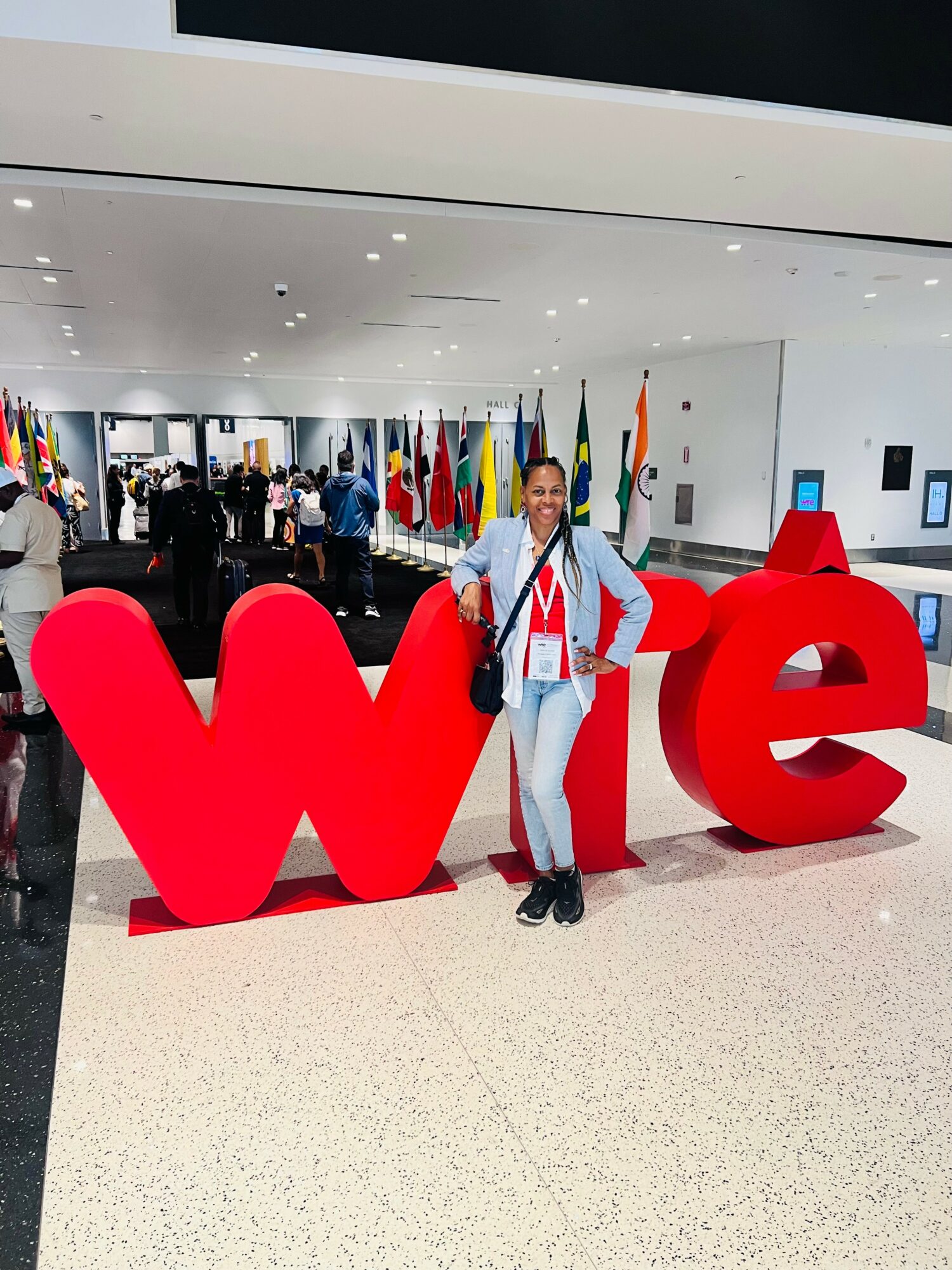Person standing next to large red letters spelling 'we' in an indoor space with flags and people in the background.