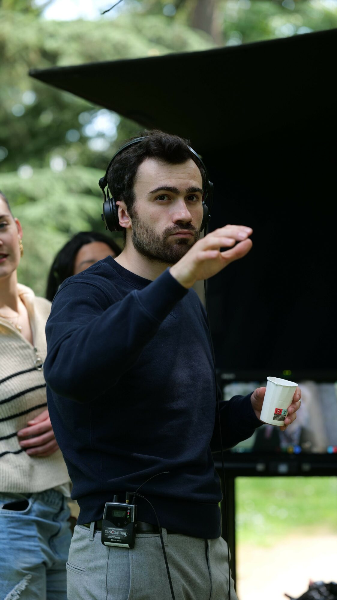 Person with dark hair and dark clothing looking at a computer screen outdoors, surrounded by trees.