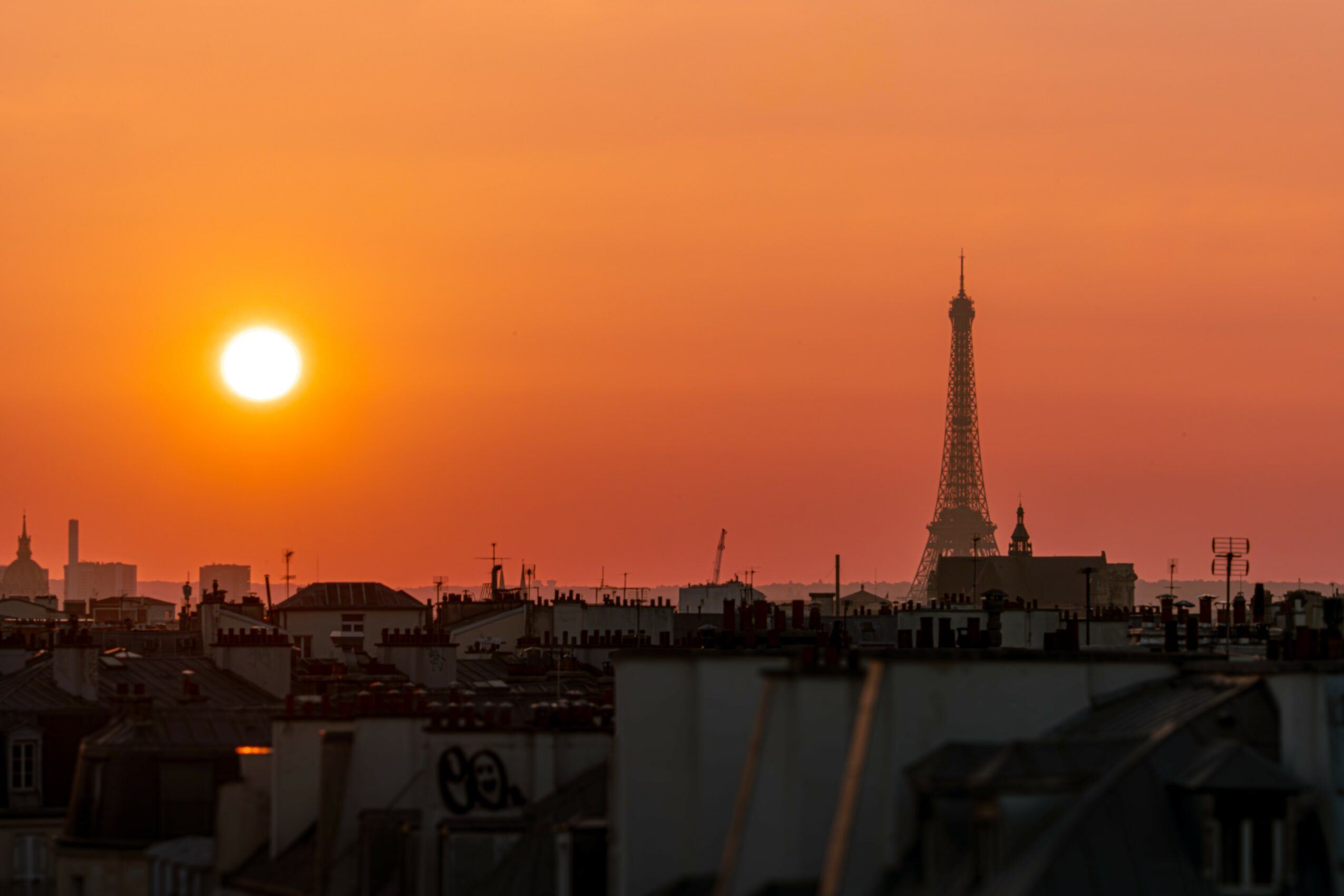 Sunset over Paris with the Eiffel Tower in the distance and city rooftops in foreground.