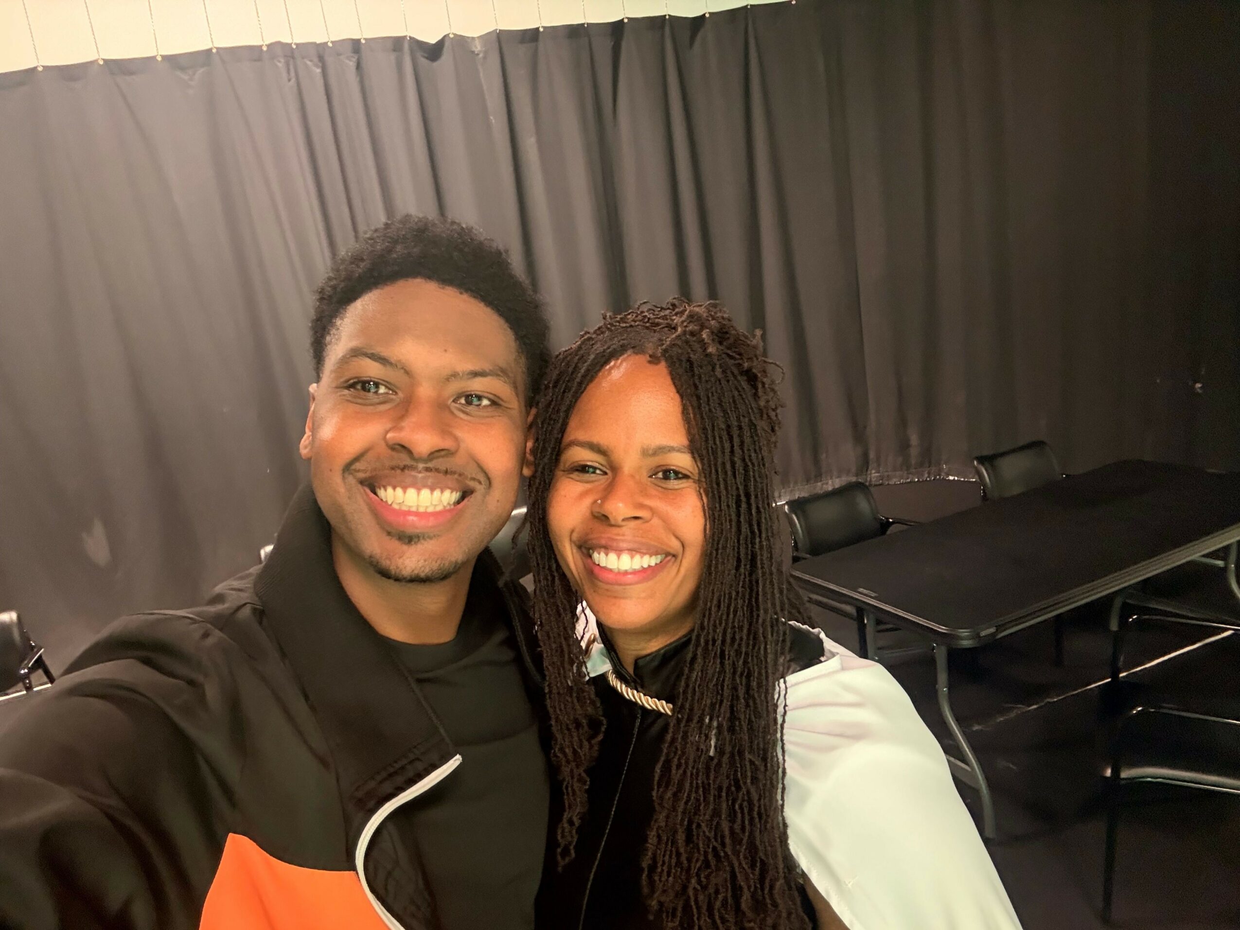 Two people smiling, upside down, with dark curtains in the background.