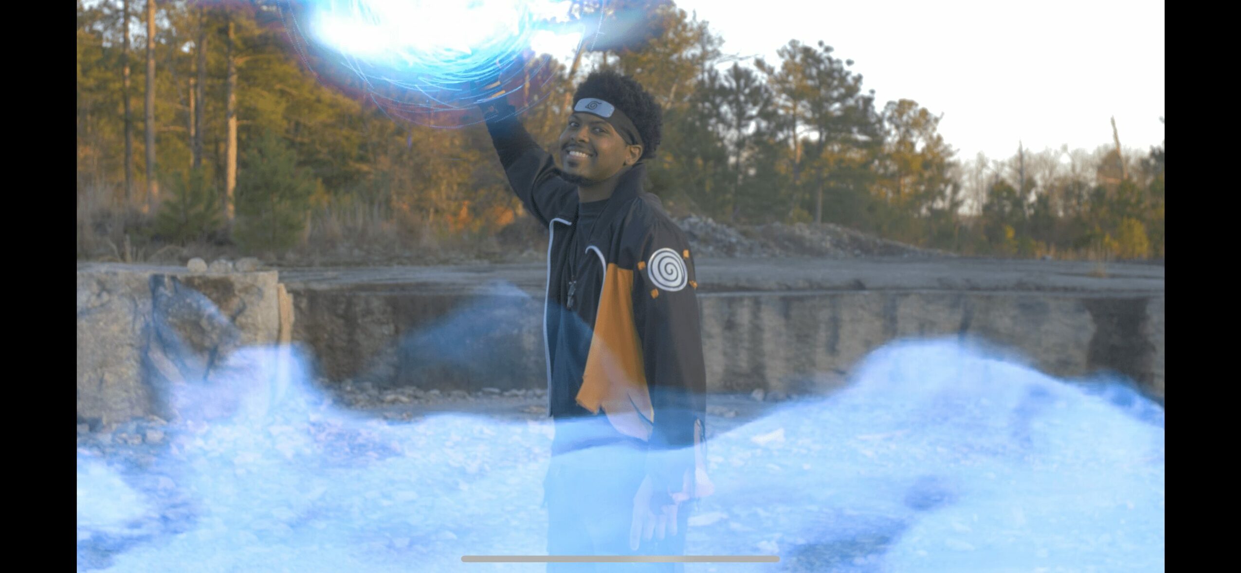 Person standing outdoors with trees in background, reaching upward with one hand, surrounded by blue mist or smoke.