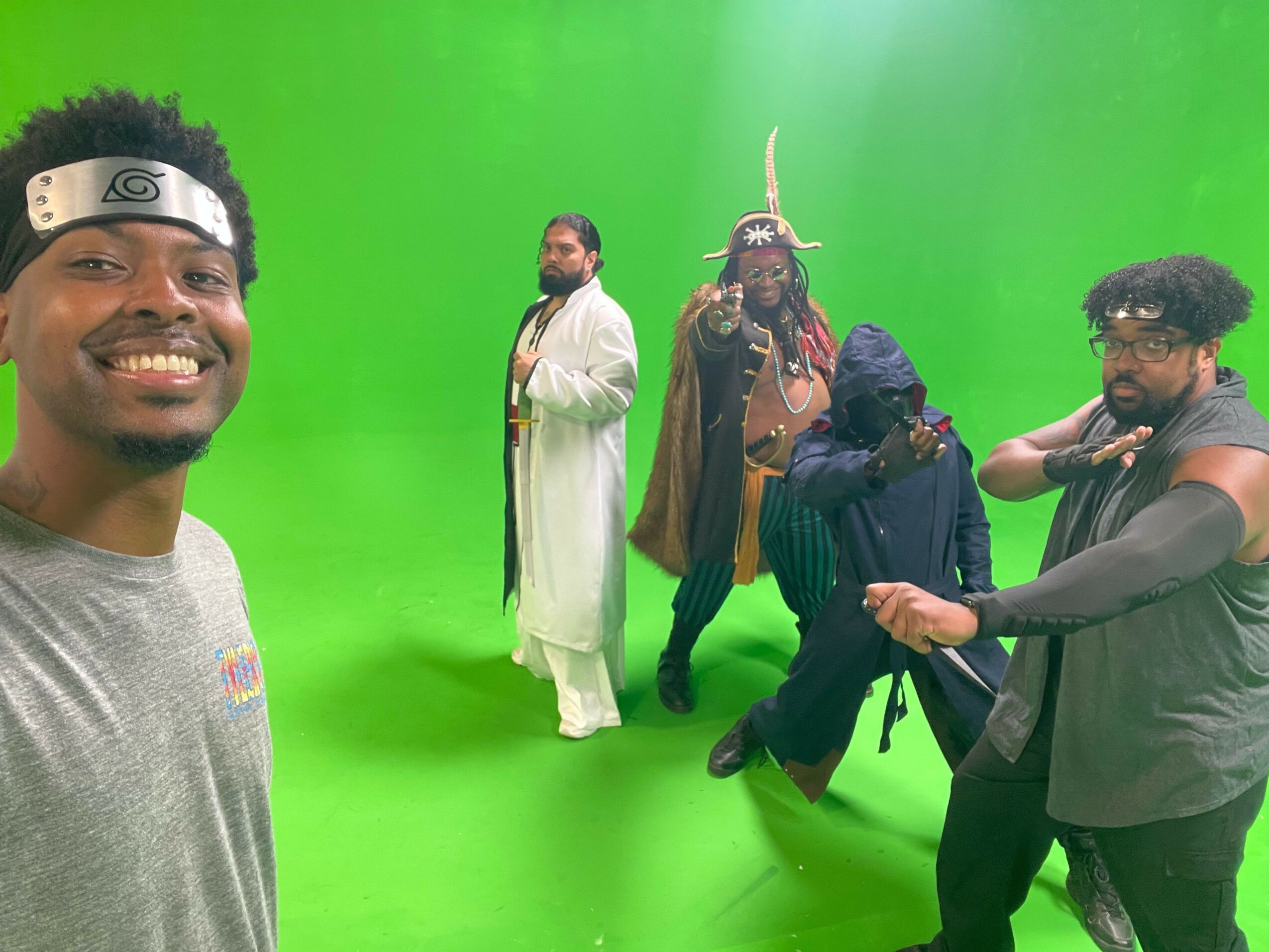 Group of five people smiling and posing in front of a green screen, some making peace signs.