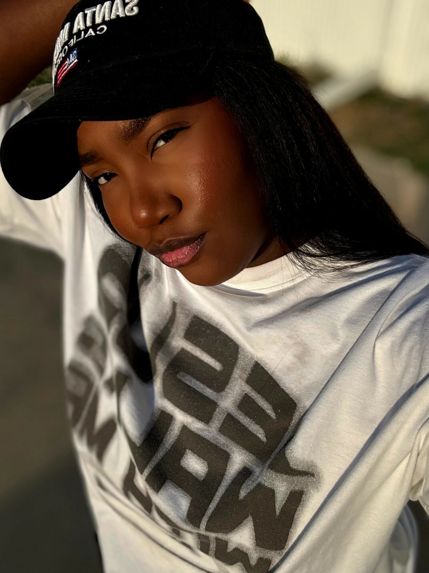 Young woman wearing a black cap and white T-shirt, looking at the camera outdoors.