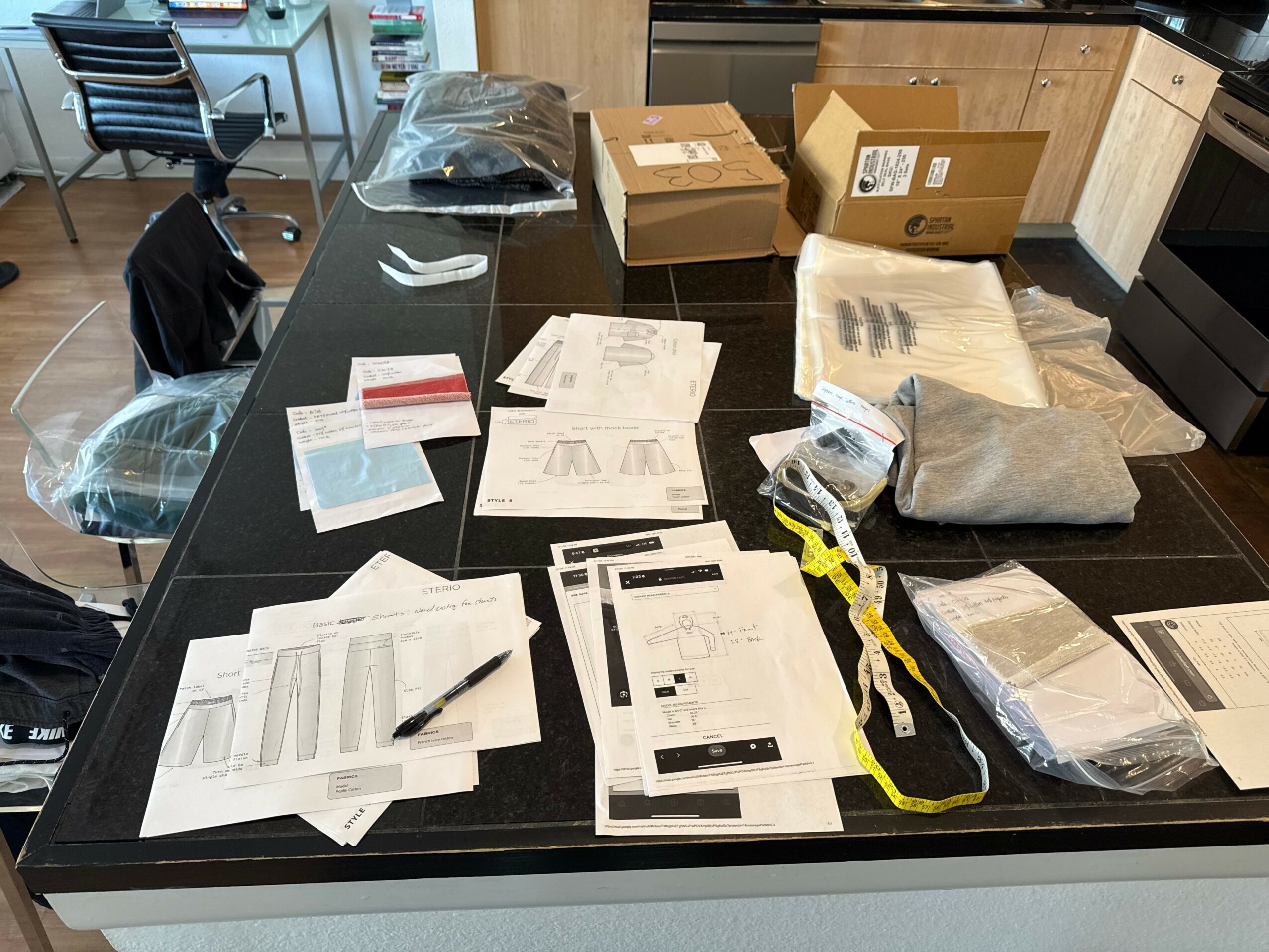 Kitchen island with papers, boxes, and bags on black countertop, kitchen cabinets in background, and a chair nearby.