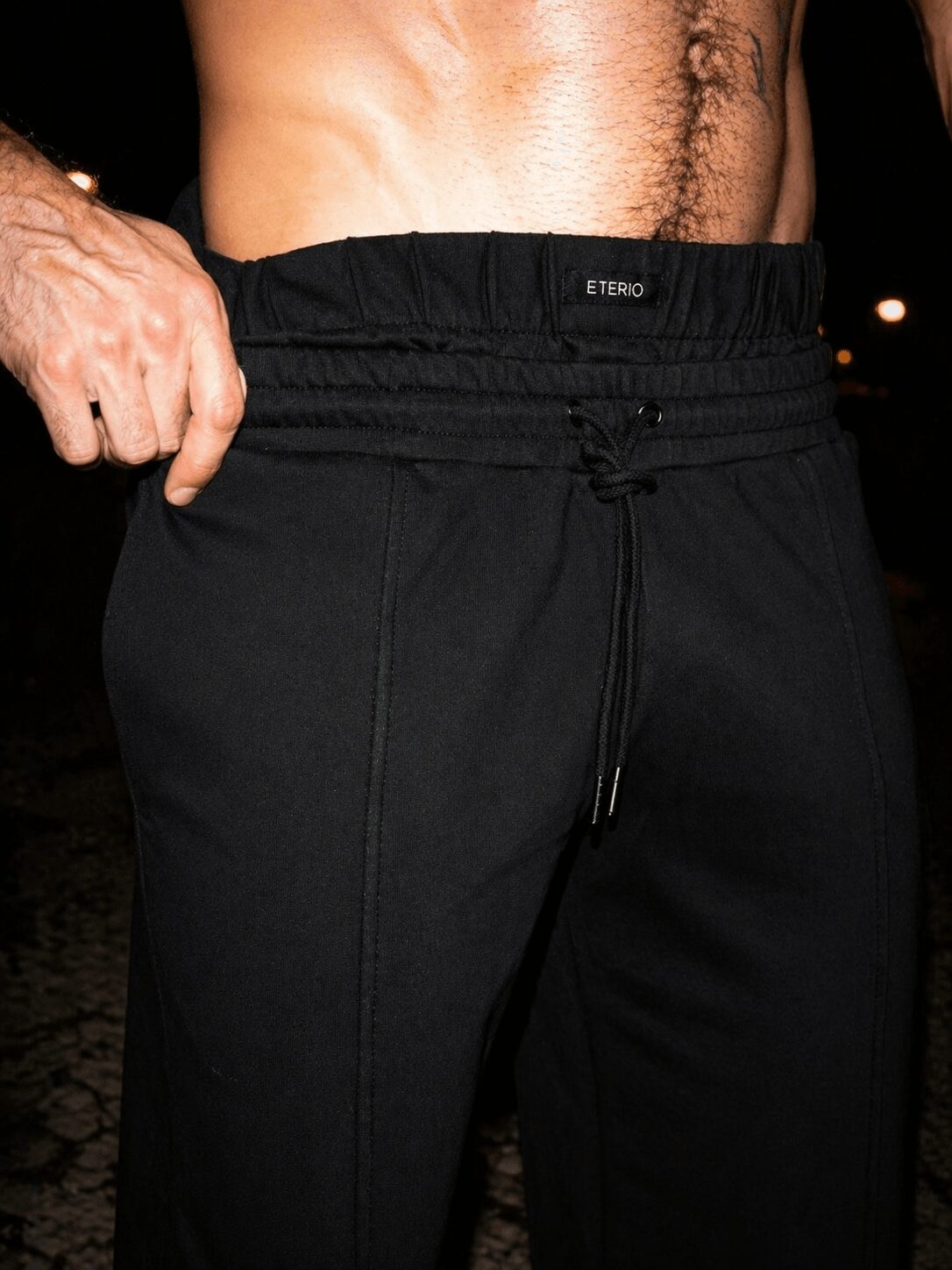 Close-up of a person's waist and hand, wearing black sweatpants with a visible waistband, outdoors at night.