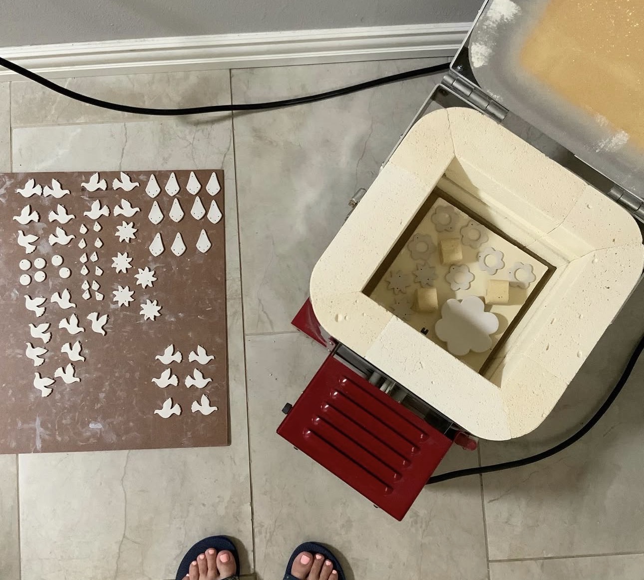 Object with small white shapes on a brown surface, viewed from above, with feet visible at the bottom, and a machine nearby.