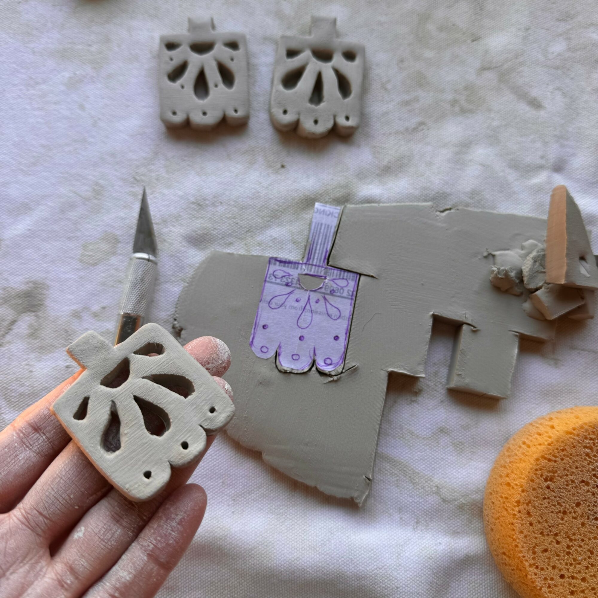 Person holding a carved soap with a floral pattern, with soap pieces and carving tools on a cloth background.