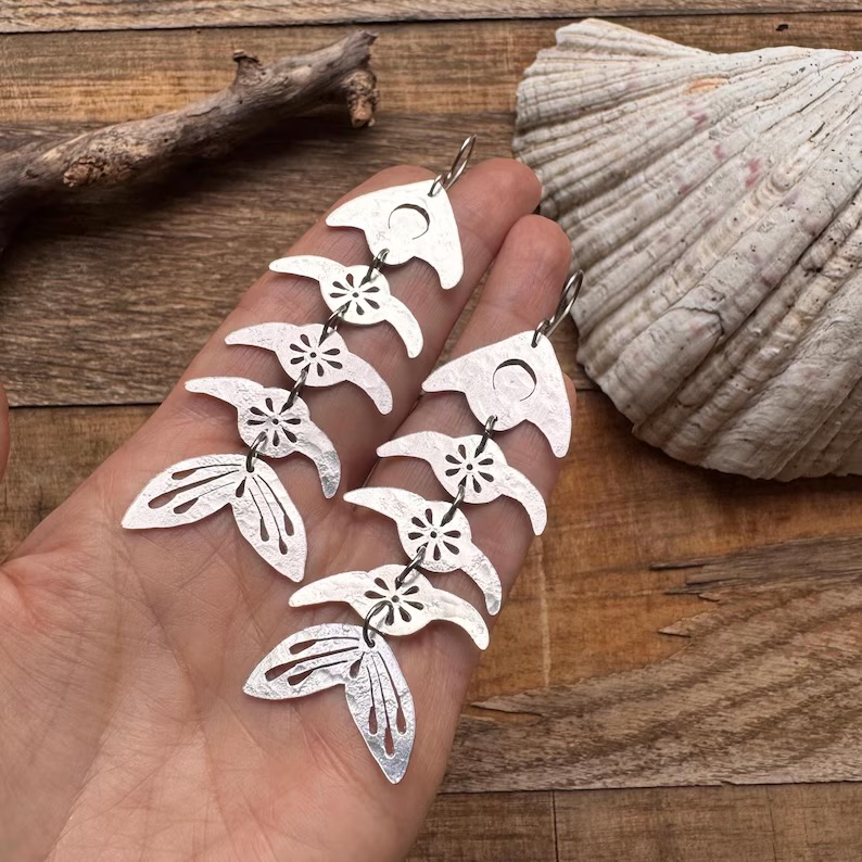 Hand holding silver butterfly and flower earrings with seashell and wooden background.