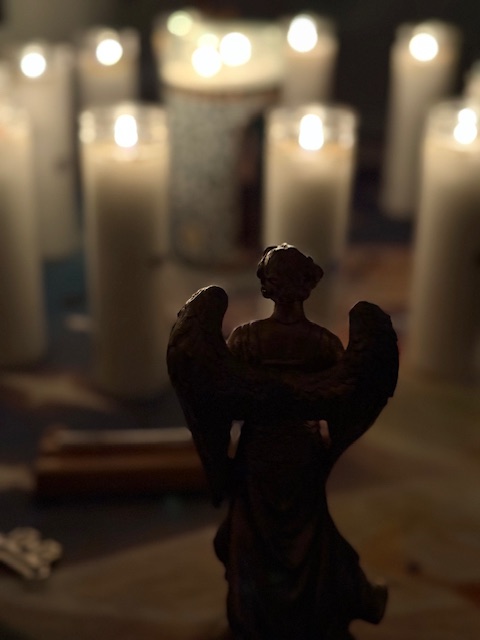 Silhouette of an angel figurine with candles in the background, creating a warm, glowing ambiance.