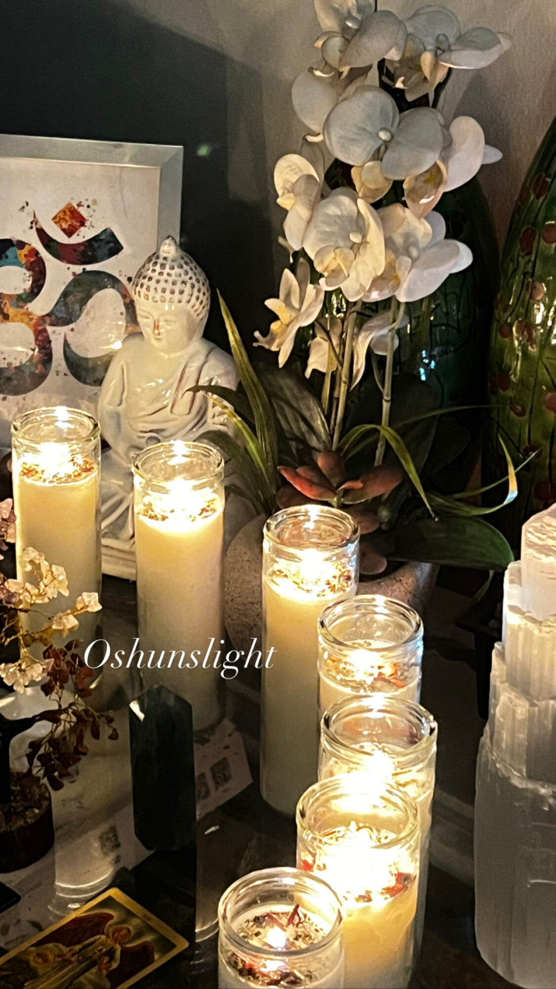 Candles, flowers, and decorative items on a table with a Buddha statue and artwork in the background.