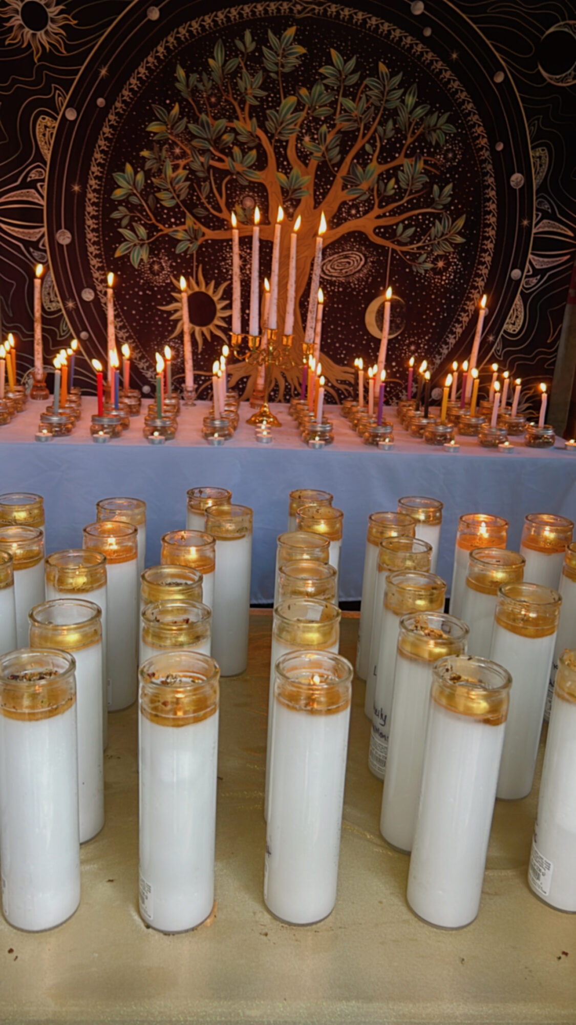 Candles arranged in front of a decorative backdrop with a tree and symbols, possibly for a ceremony or celebration.