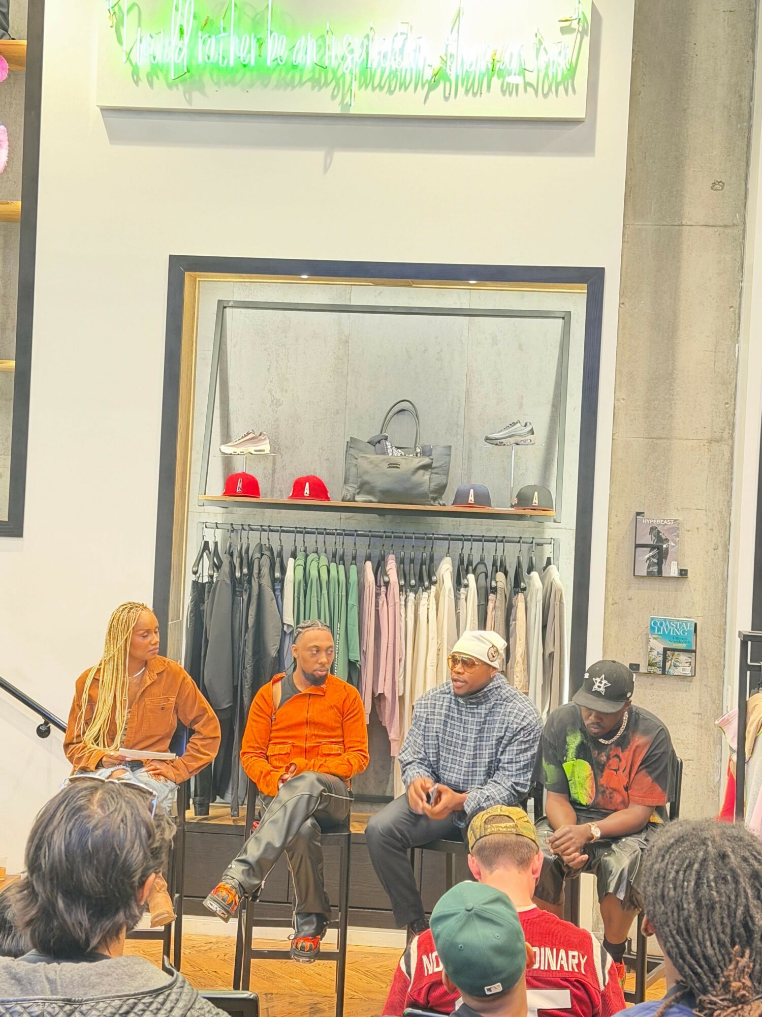 People gather around a display case with clothing items inside, some wearing masks and colorful clothing, in an indoor setting.