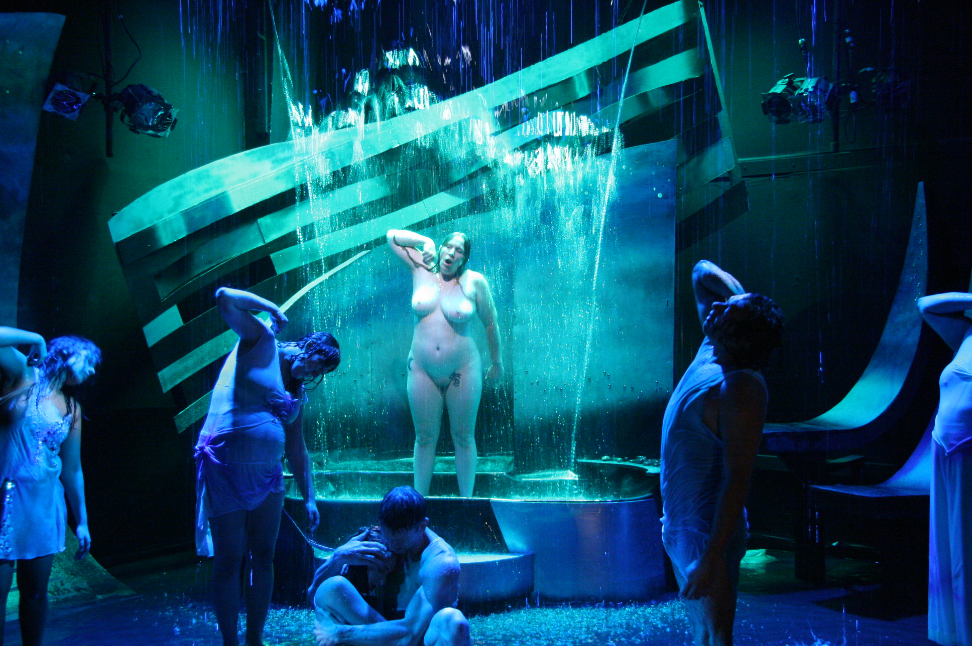 Group of children around a fountain with a statue of a woman, illuminated by blue and green lights, in an indoor setting.