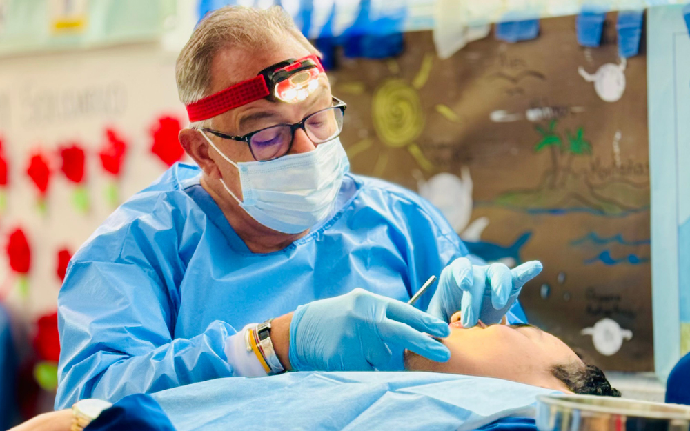 A healthcare professional wearing a mask, gloves, and protective gown performs a medical procedure on a patient.