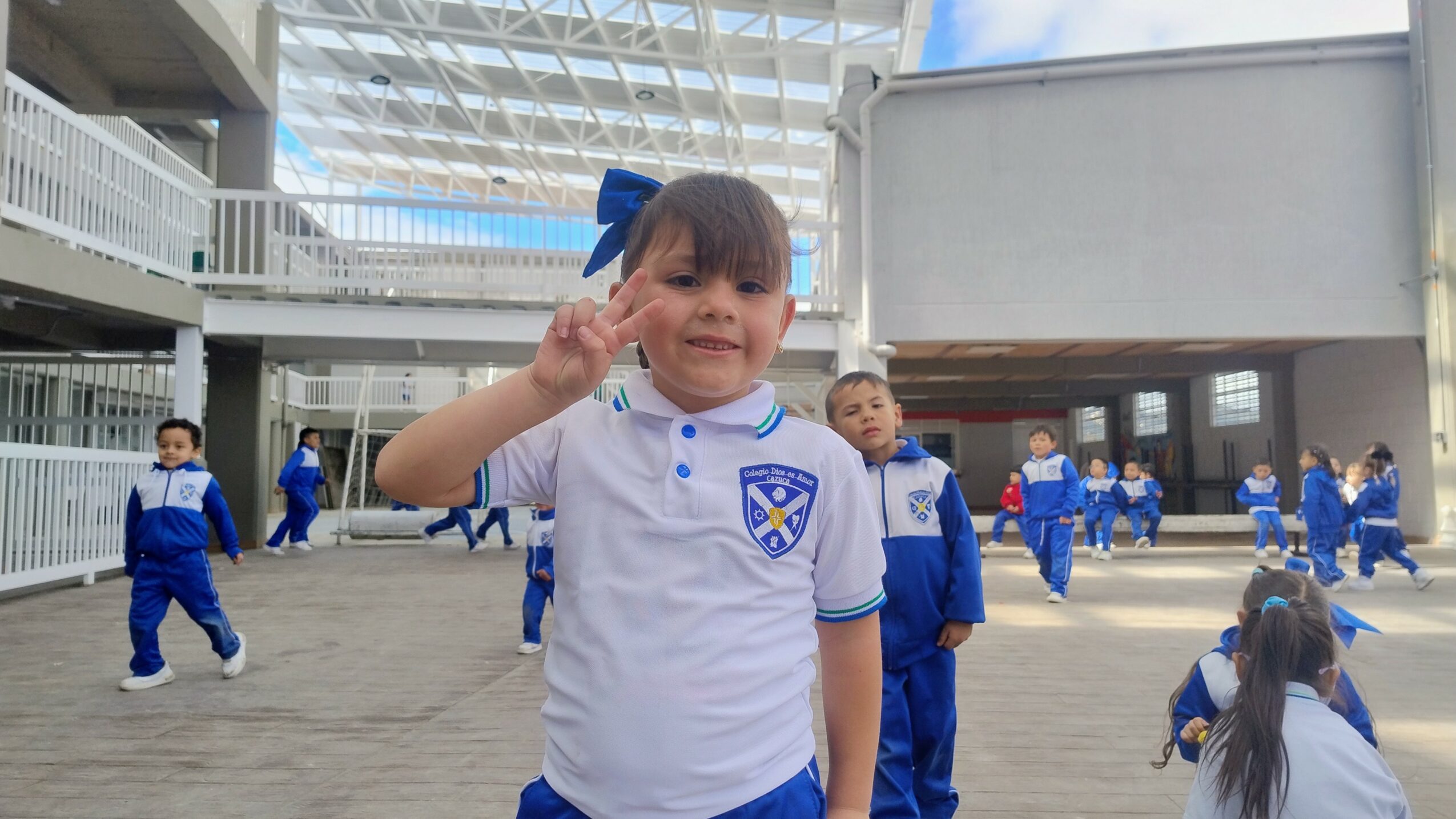 Young girl in school uniform making a peace sign, surrounded by children in similar uniforms outside a school building.