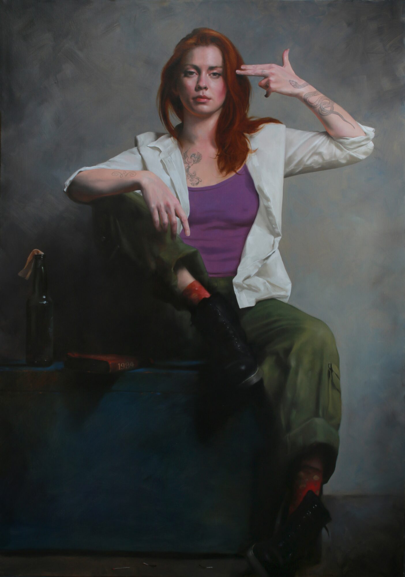 Young woman with red hair sitting on a box, making a gesture with her hand, wearing a purple top and green pants.
