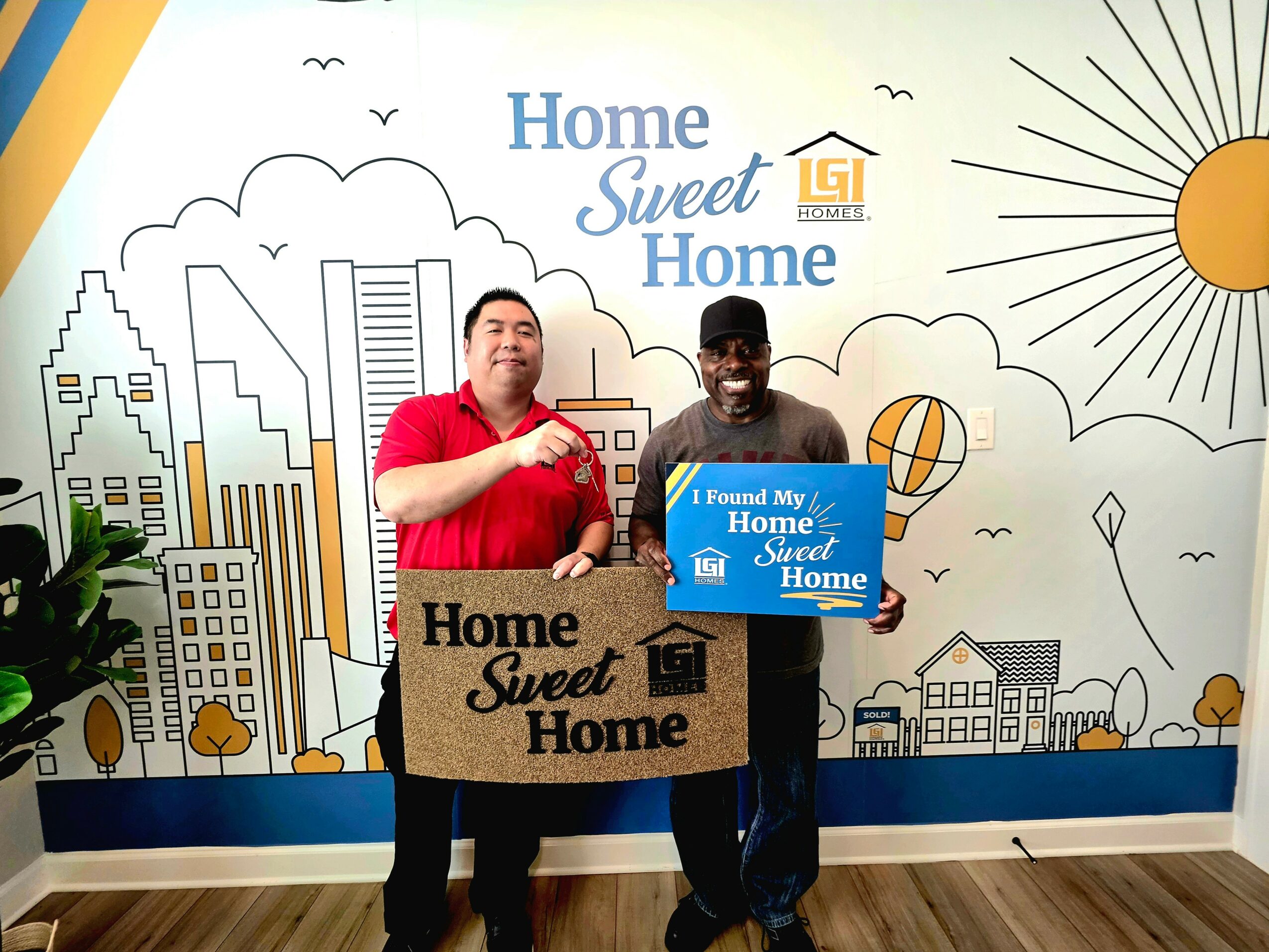 Two men holding signs in front of a colorful cityscape mural with the text 'Home Sweet Home' and a sun illustration.