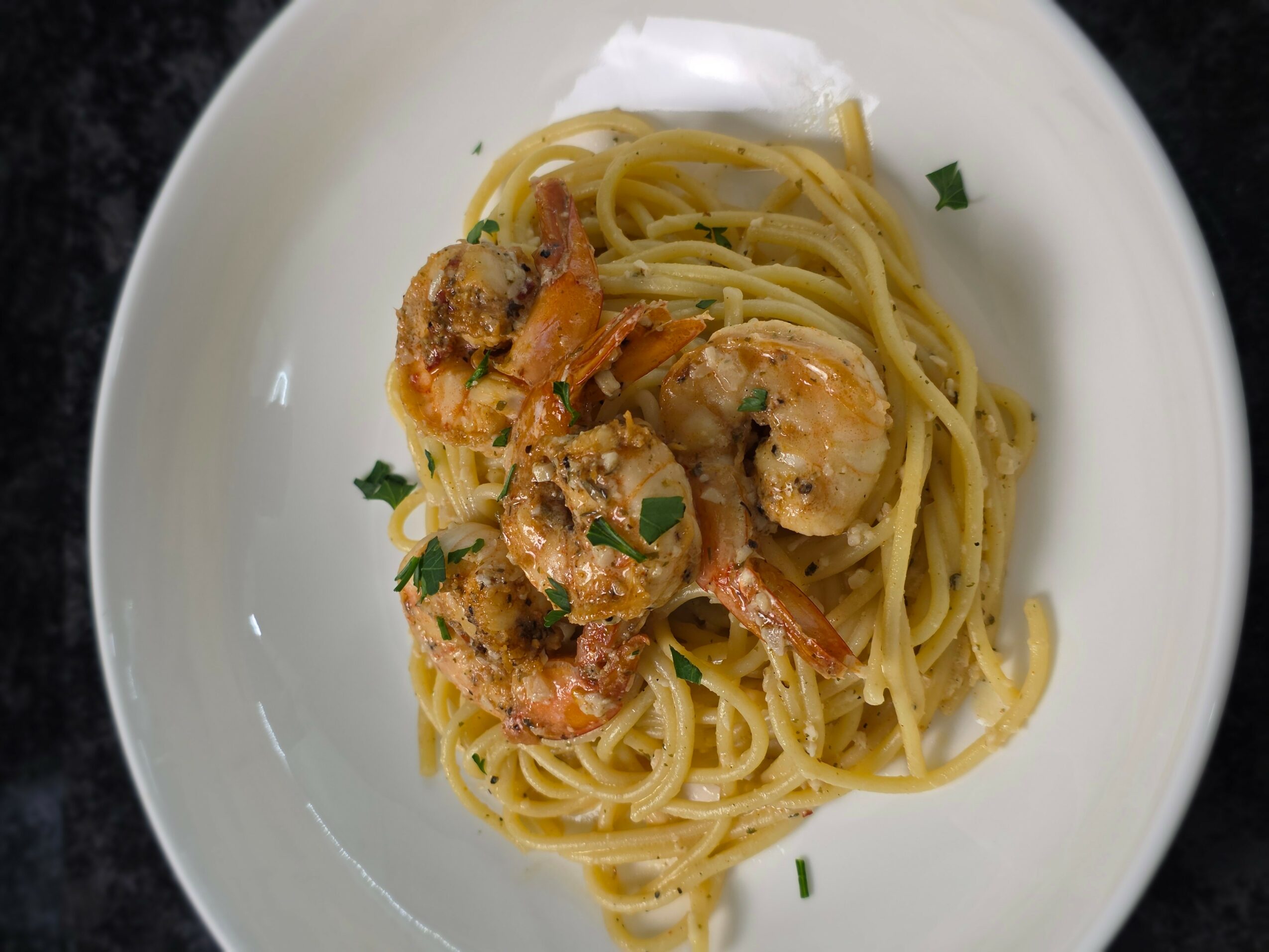 Plate of spaghetti with shrimp and green herbs, served on a white dish.
