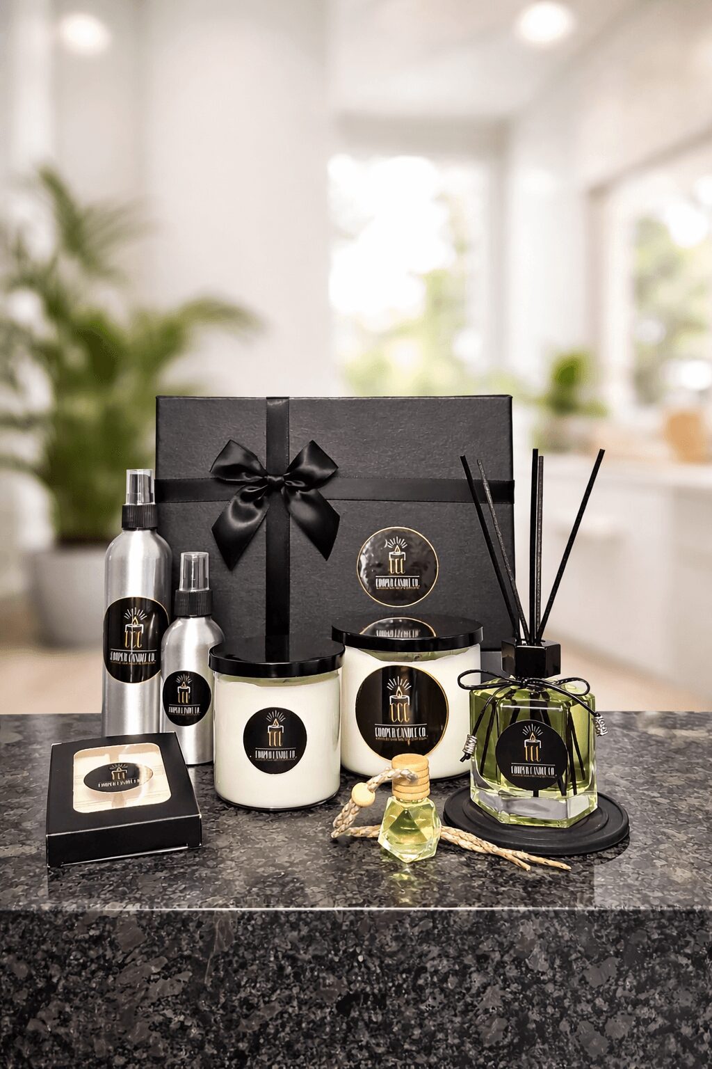 Collection of black and white luxury gift items, including candles, a box, and a reed diffuser, on a kitchen counter.
